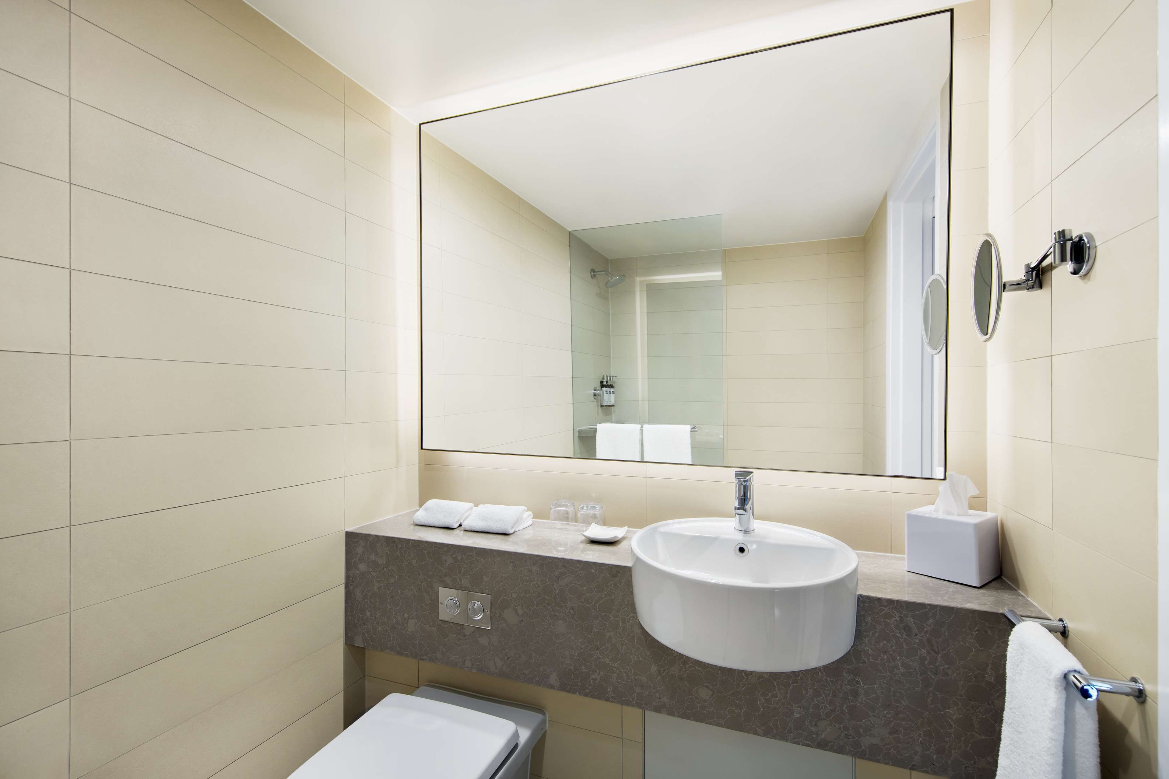 A modern bathroom with a large mirror, a sink, and a toilet.