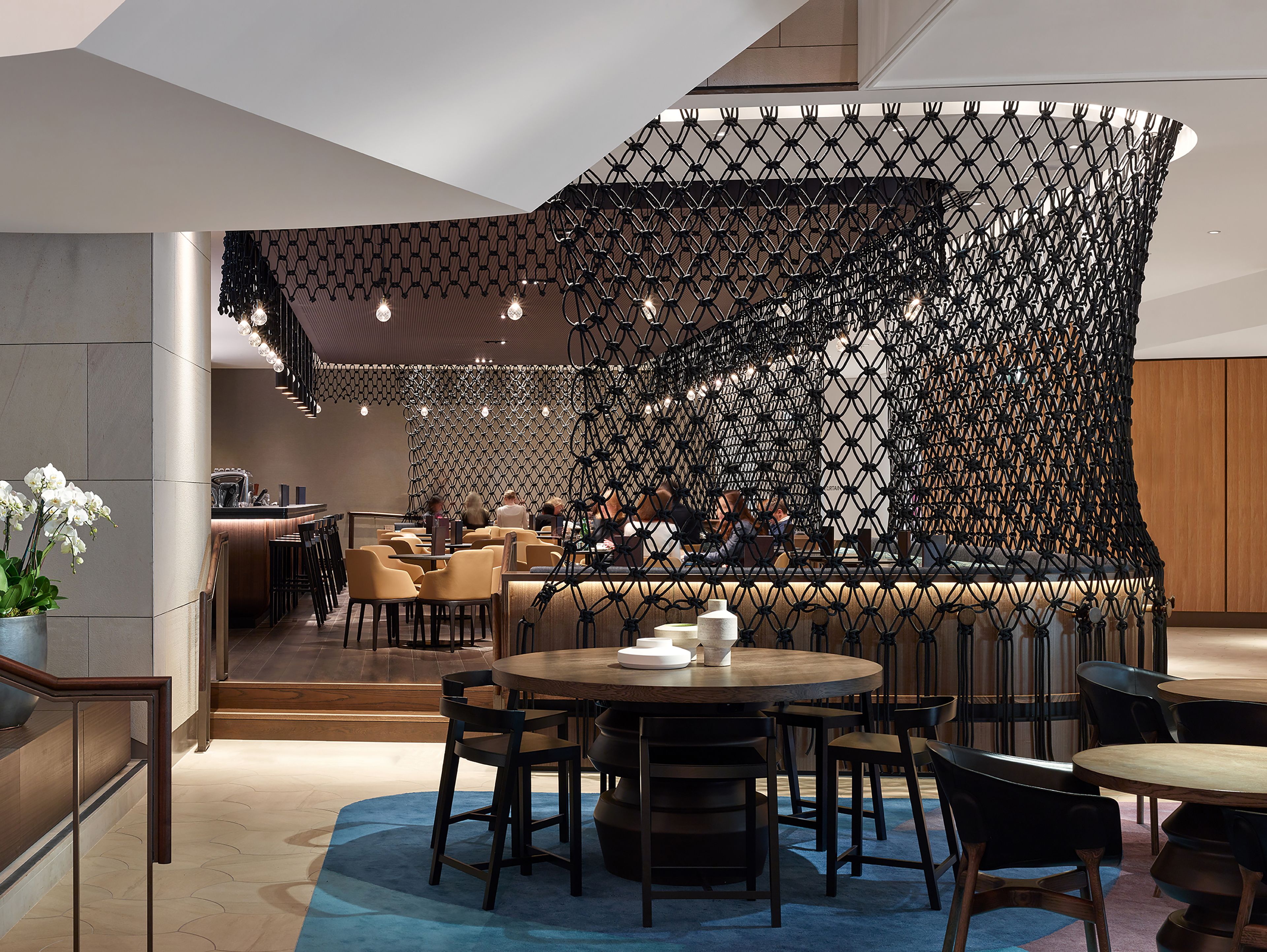 A modern restaurant with a unique black netted partition, wooden tables, and chairs.