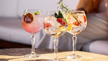 Trois verres de cocktails, avec glaçons et décorations, posés sur une table en bois.