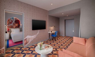 Una moderna camera d'hotel con un letto grande, una televisione a parete, una scrivania con una sedia e un pavimento decorato.