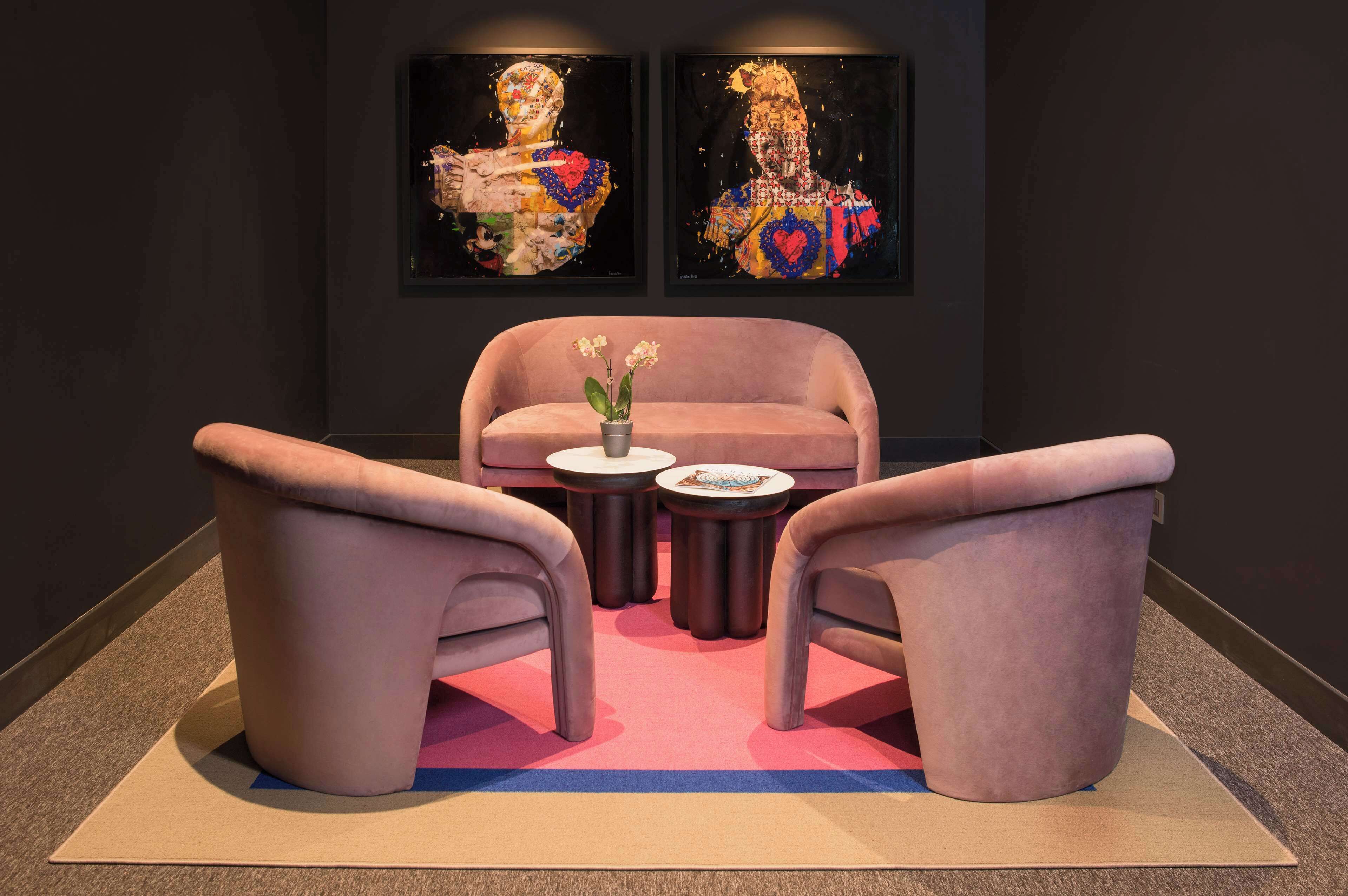 Een kamer met een roze bank, twee fauteuils, een bijzettafeltje met een bloevas en twee ingelijste kunstwerken aan de muur.