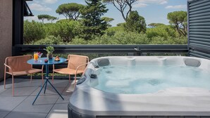 Un bain à remous sur un balcon, agrémenté de chaises et d’une table, le tout entouré de verdure et d’arbres.