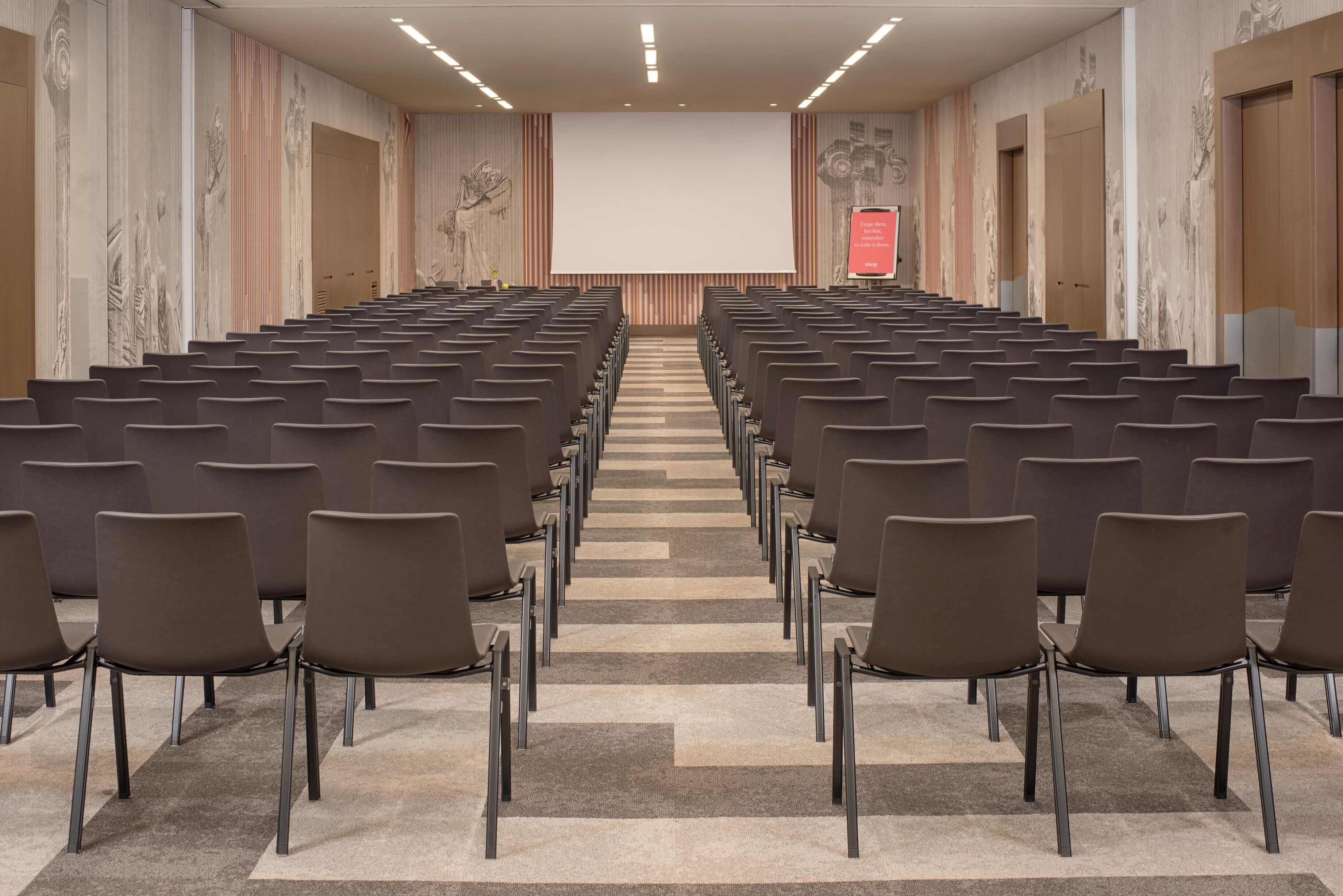 A conference room with rows of chairs facing a large screen and a podium.