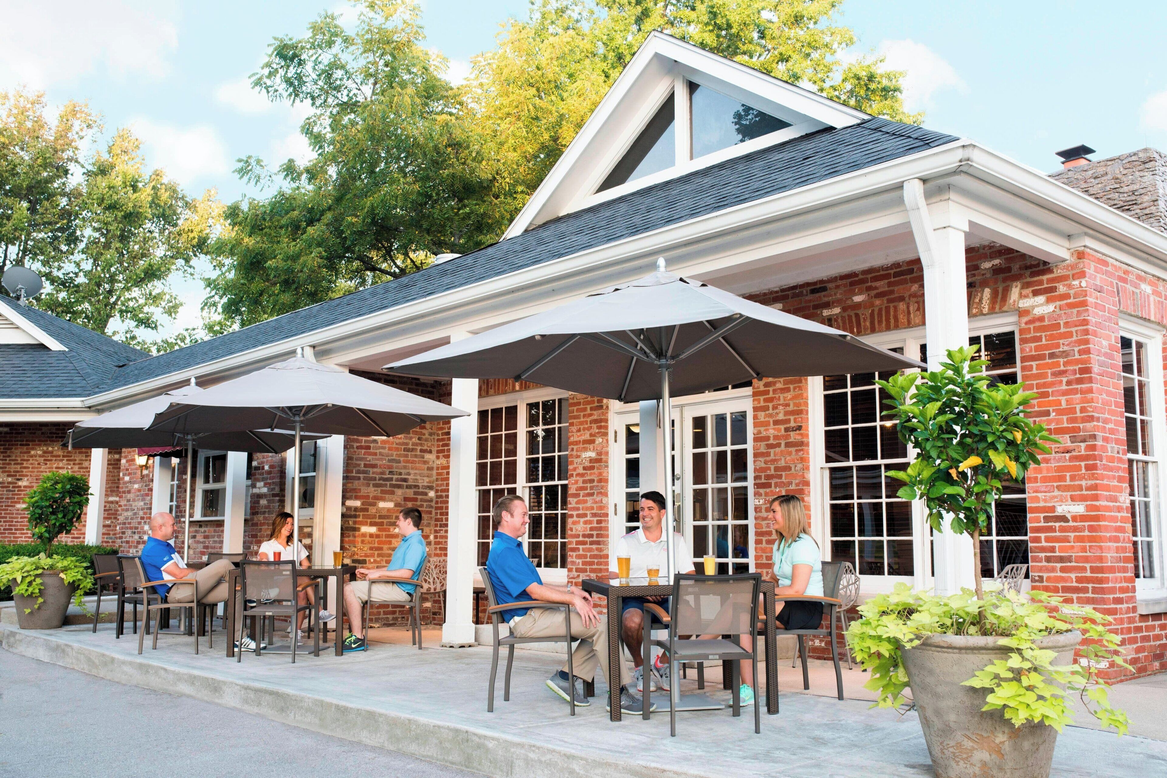 Ein Terrassenbereich im Freien mit Ziegelmauern, großen Fenstern und Sitzgelegenheiten unter Sonnenschirmen.