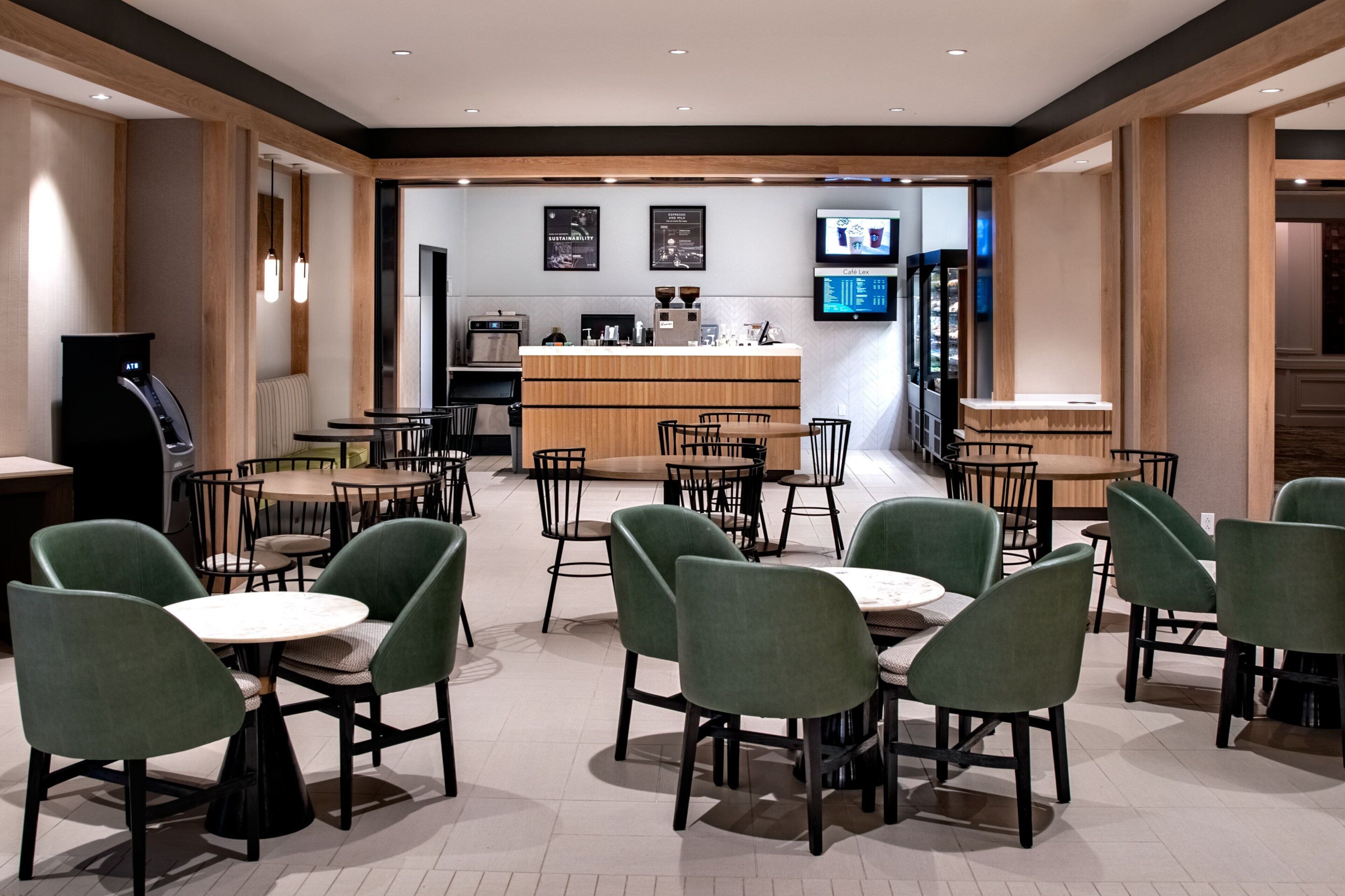 A modern cafe with round tables and green chairs, a coffee machine, and a counter with a menu.