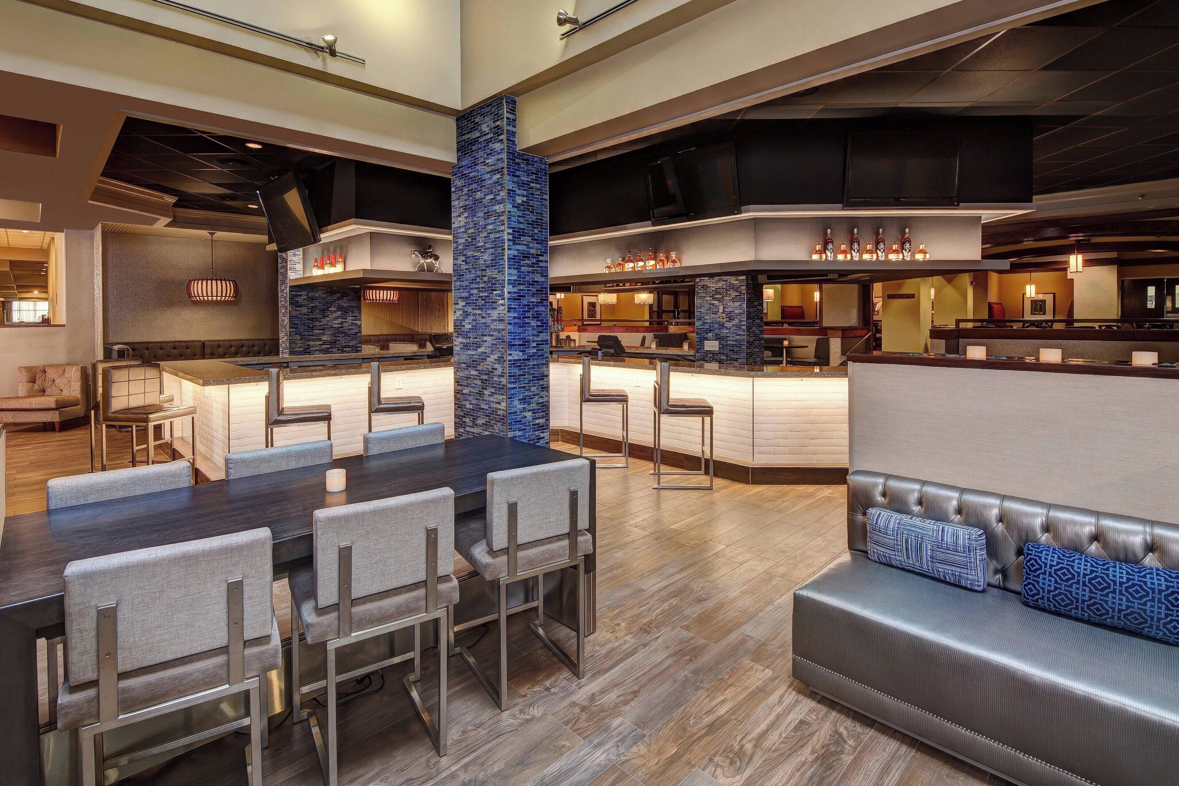 A modern hotel lobby with a dining area, a bar, and a seating area.
