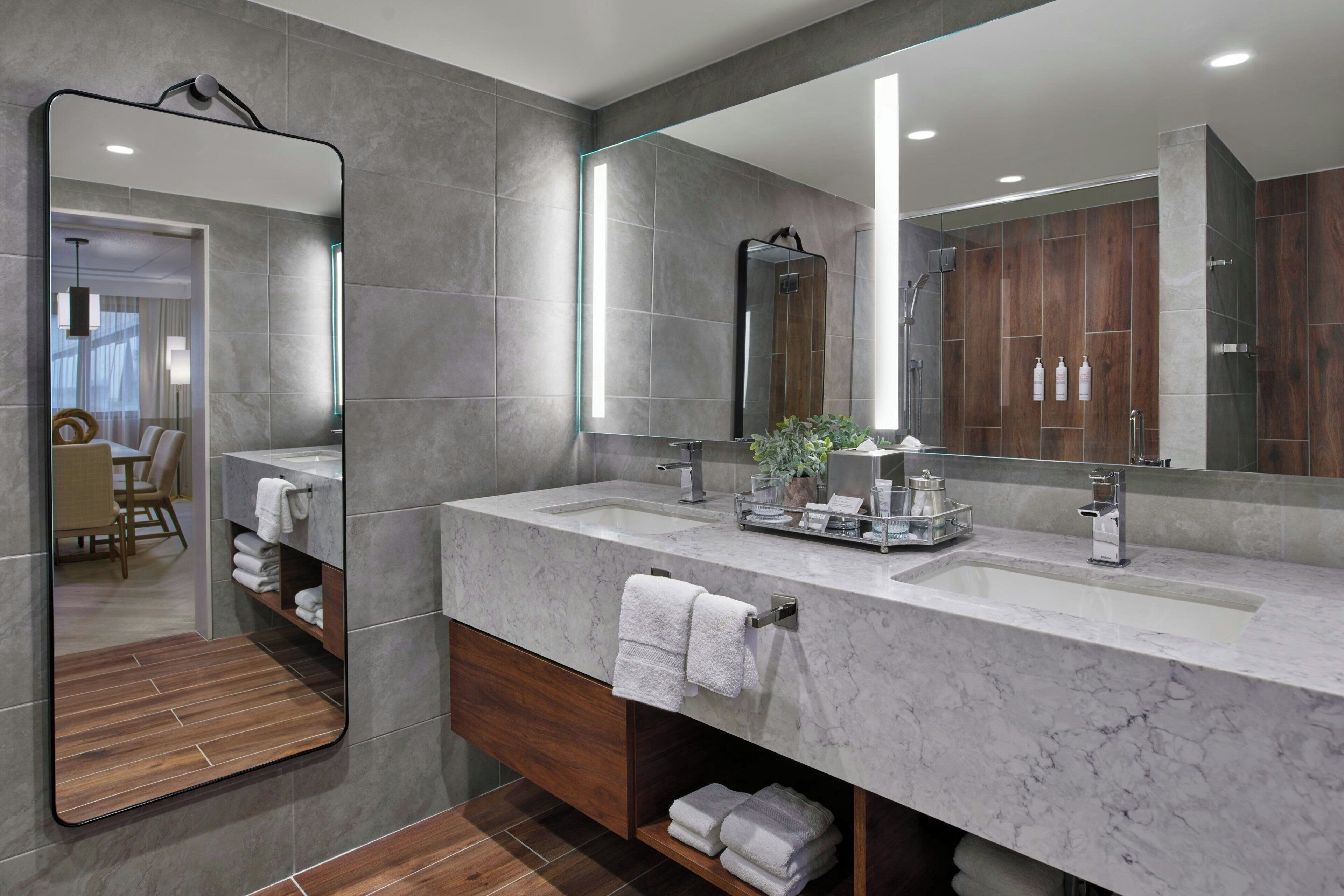 A modern bathroom with a large mirror, two sinks, and a vanity with shelves for towels.