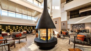 A modern lobby with a central glass fireplace, seating areas, and a high ceiling with natural light. - Marriott Lexington Griffin Gate Golf Resort & Spa (Lexington)