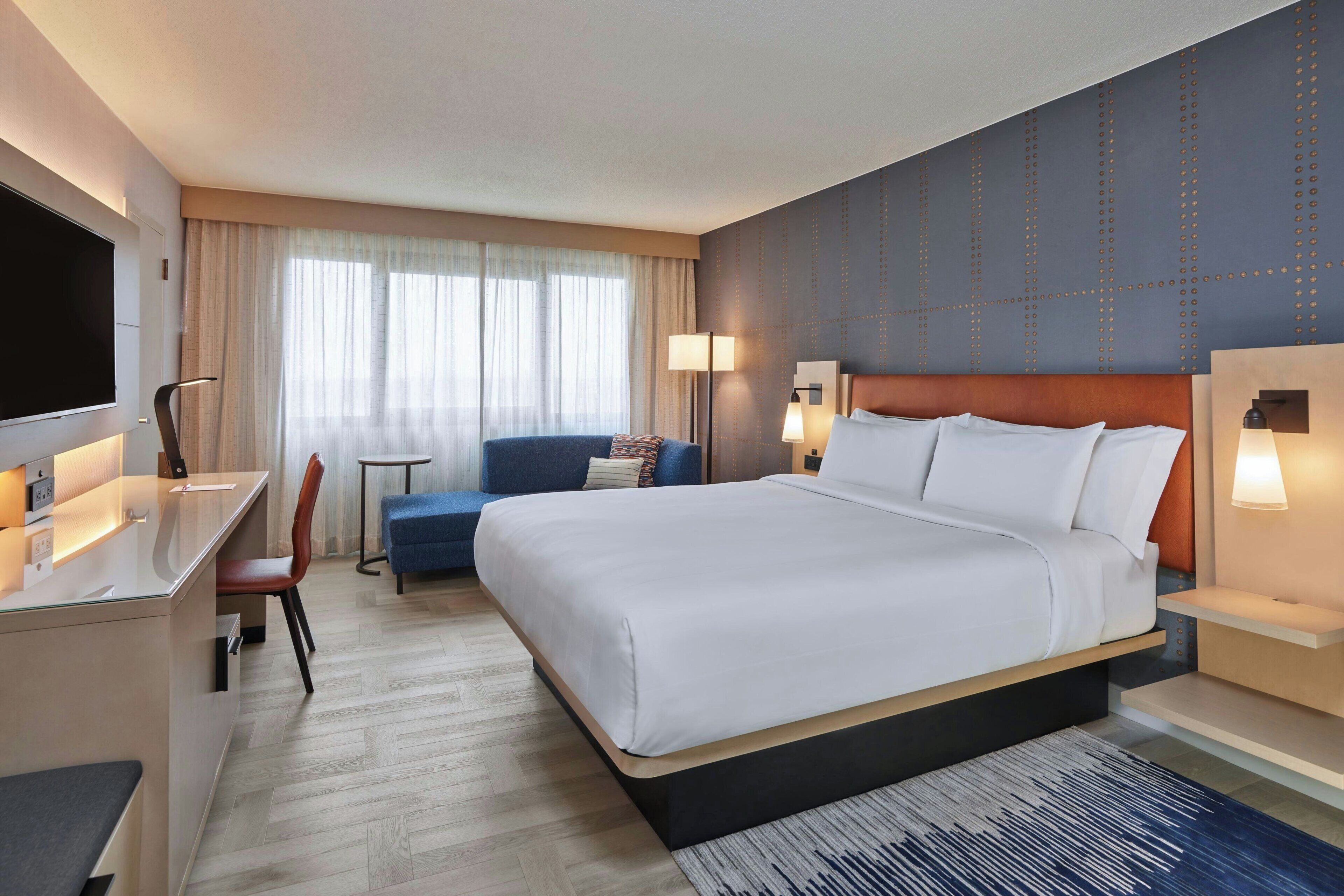 Ein Hotelzimmer mit einem großen Bett, einem Schreibtisch mit Stuhl, einer Couch und einem Fernseher.