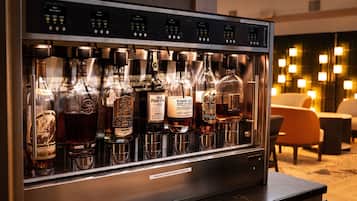 Een drankkoelkast gevuld met diverse flessen drank, een digitaal bedieningspaneel en een bordje met de tekst: voor meer informatie, neem contact op met de bar.