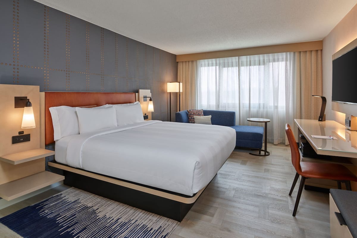 A hotel room with a large bed, a desk, a chair, a sofa, and a TV.