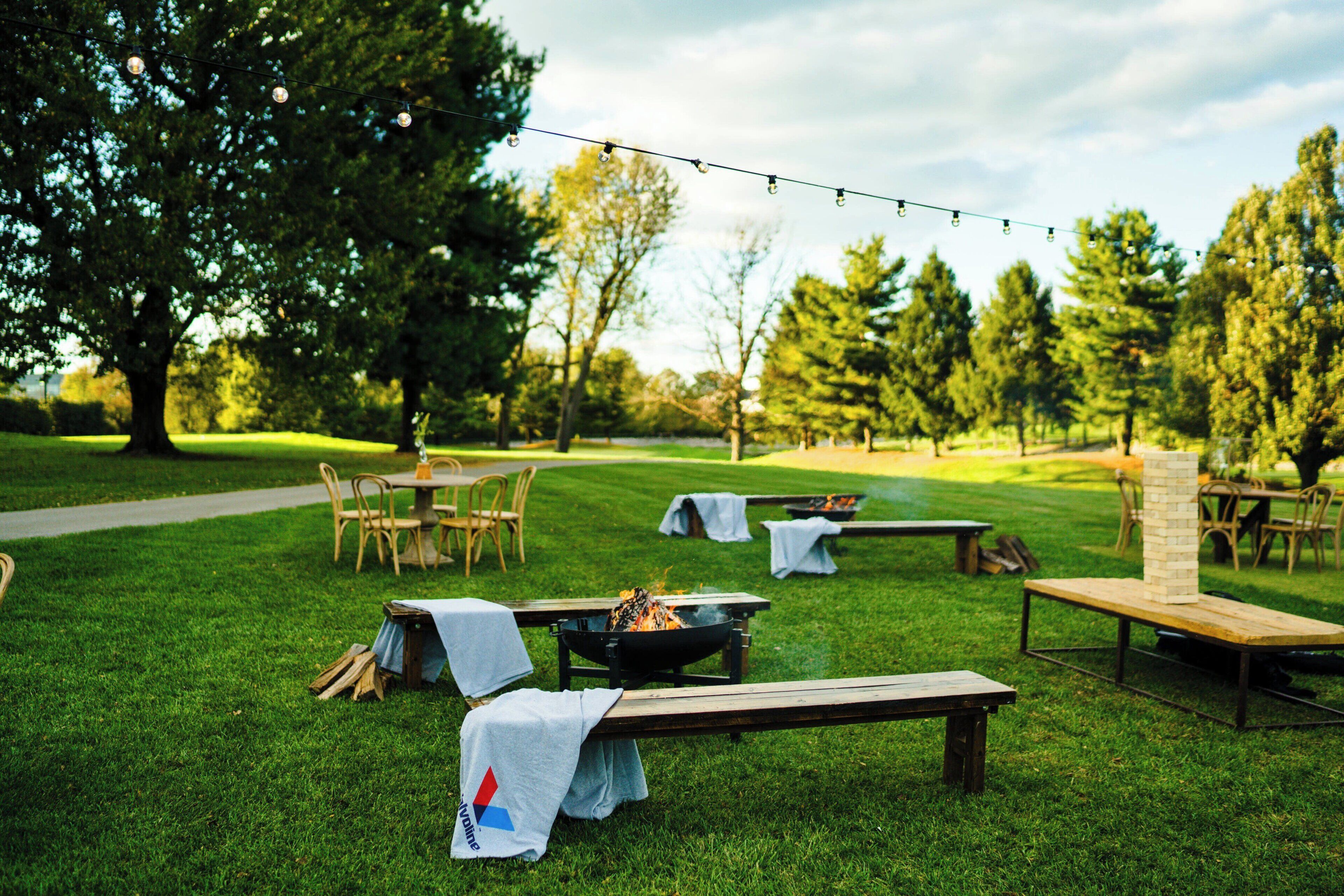 An outdoor setting with picnic tables, a fire pit, and string lights.