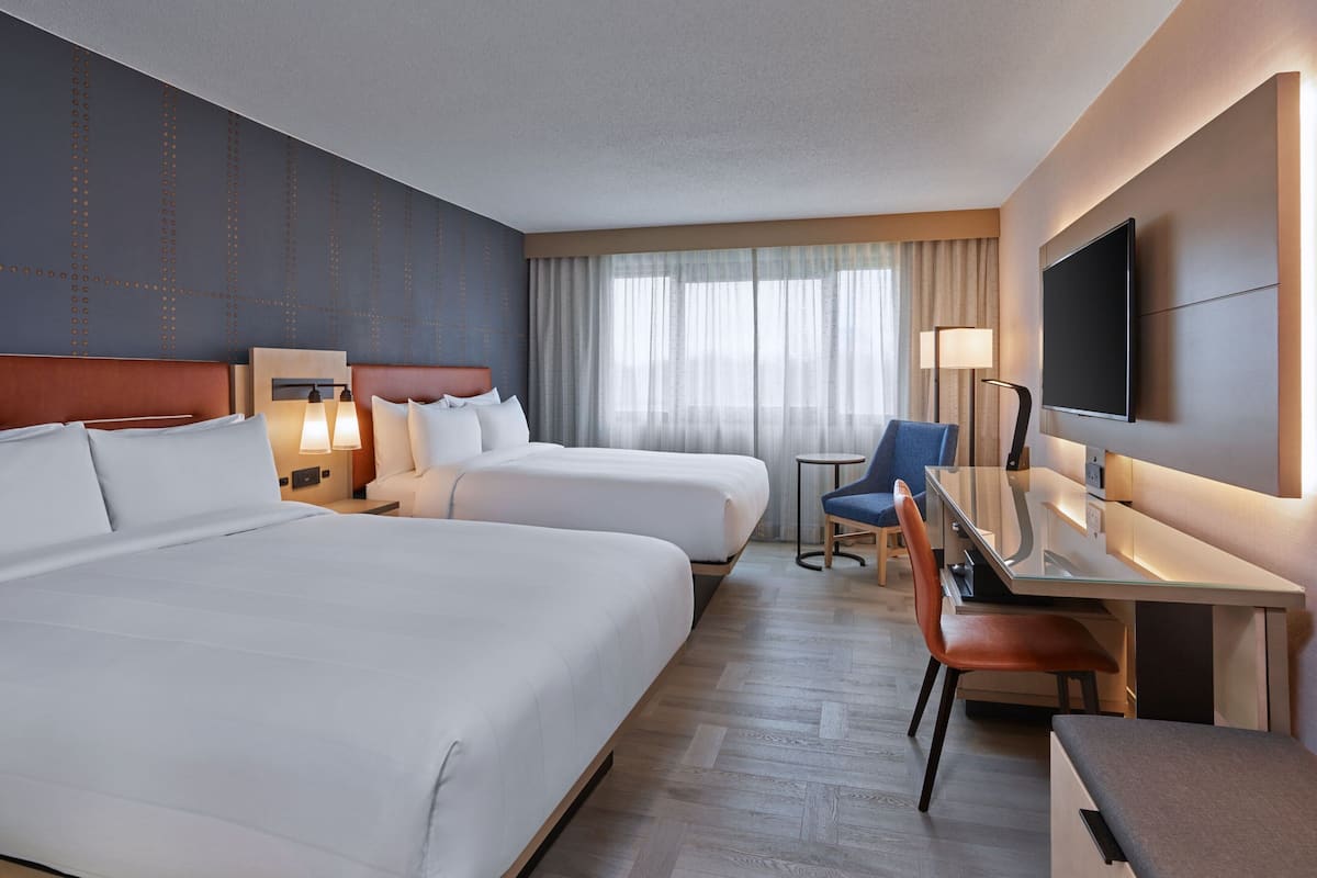 A hotel room with two beds, a desk with a chair, a TV, and a window with curtains.