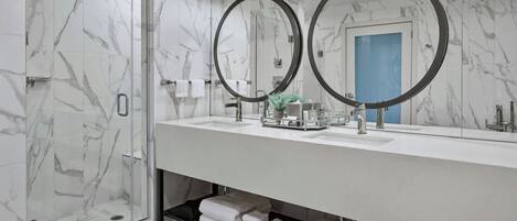 A modern bathroom with a glass-enclosed shower, a large mirror with two circular frames, and a white vanity with a sink and towel storage.