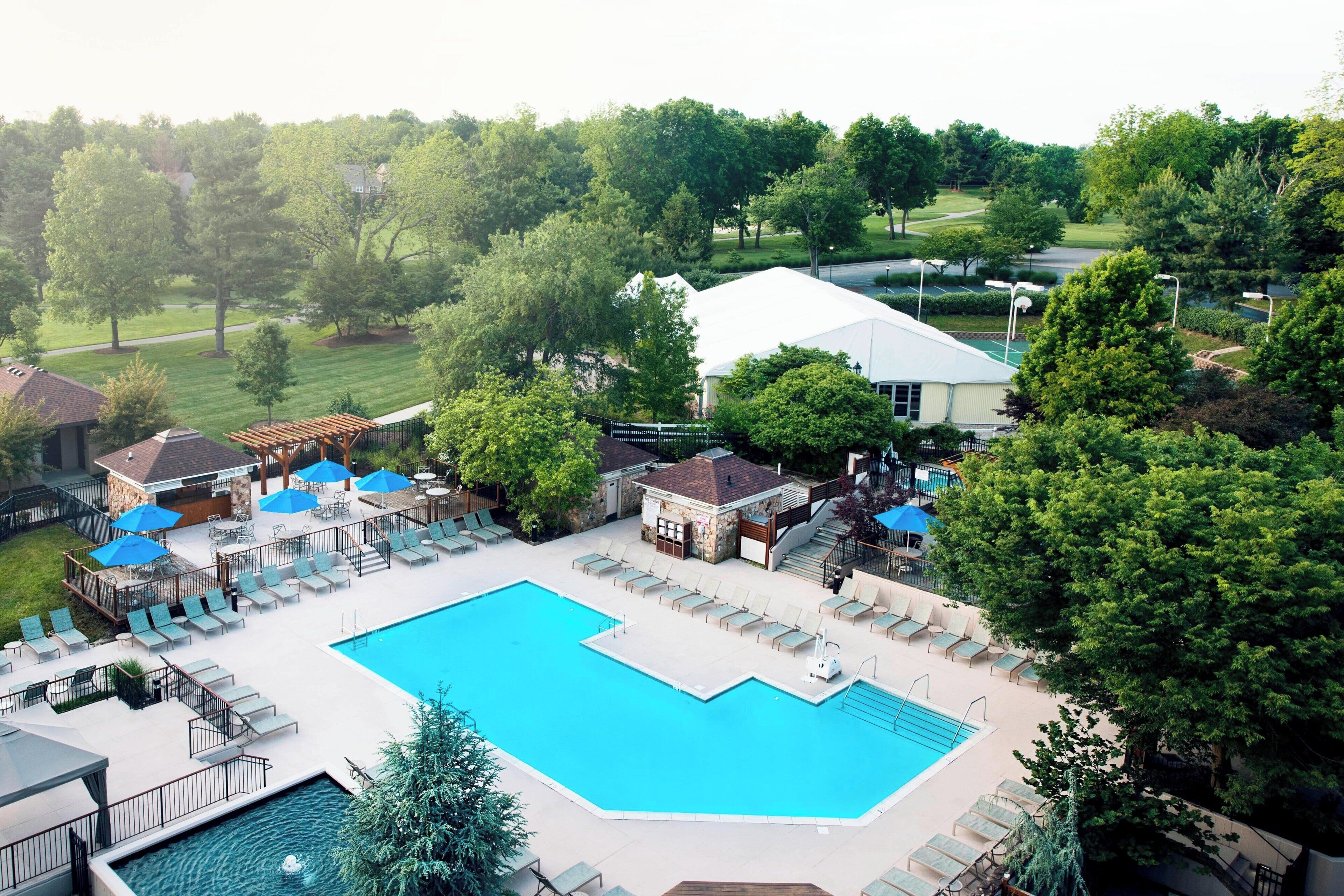 A swimming pool with lounge chairs and umbrellas, surrounded by trees and a building.