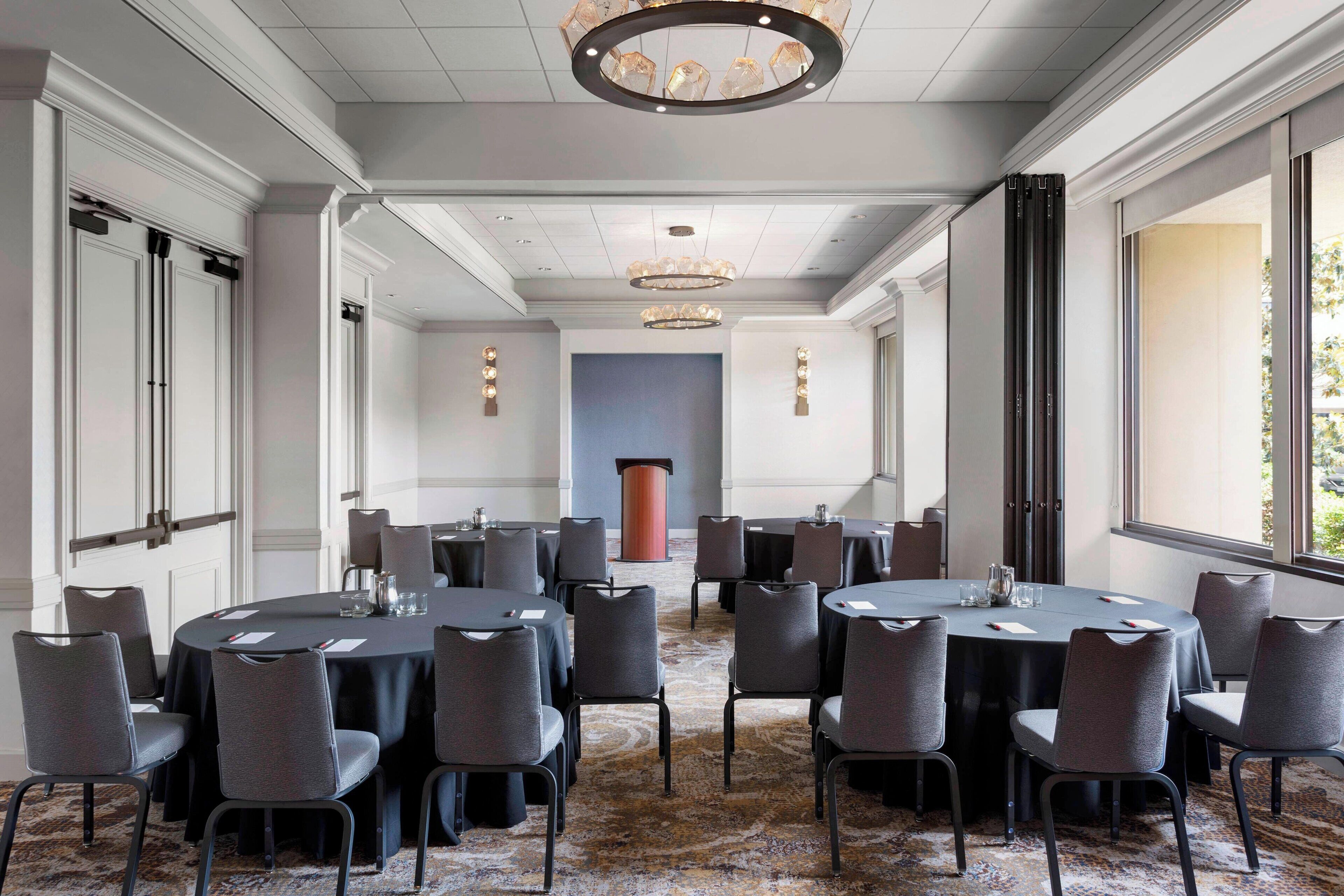 A conference room with round tables and chairs, a podium, and a large window.