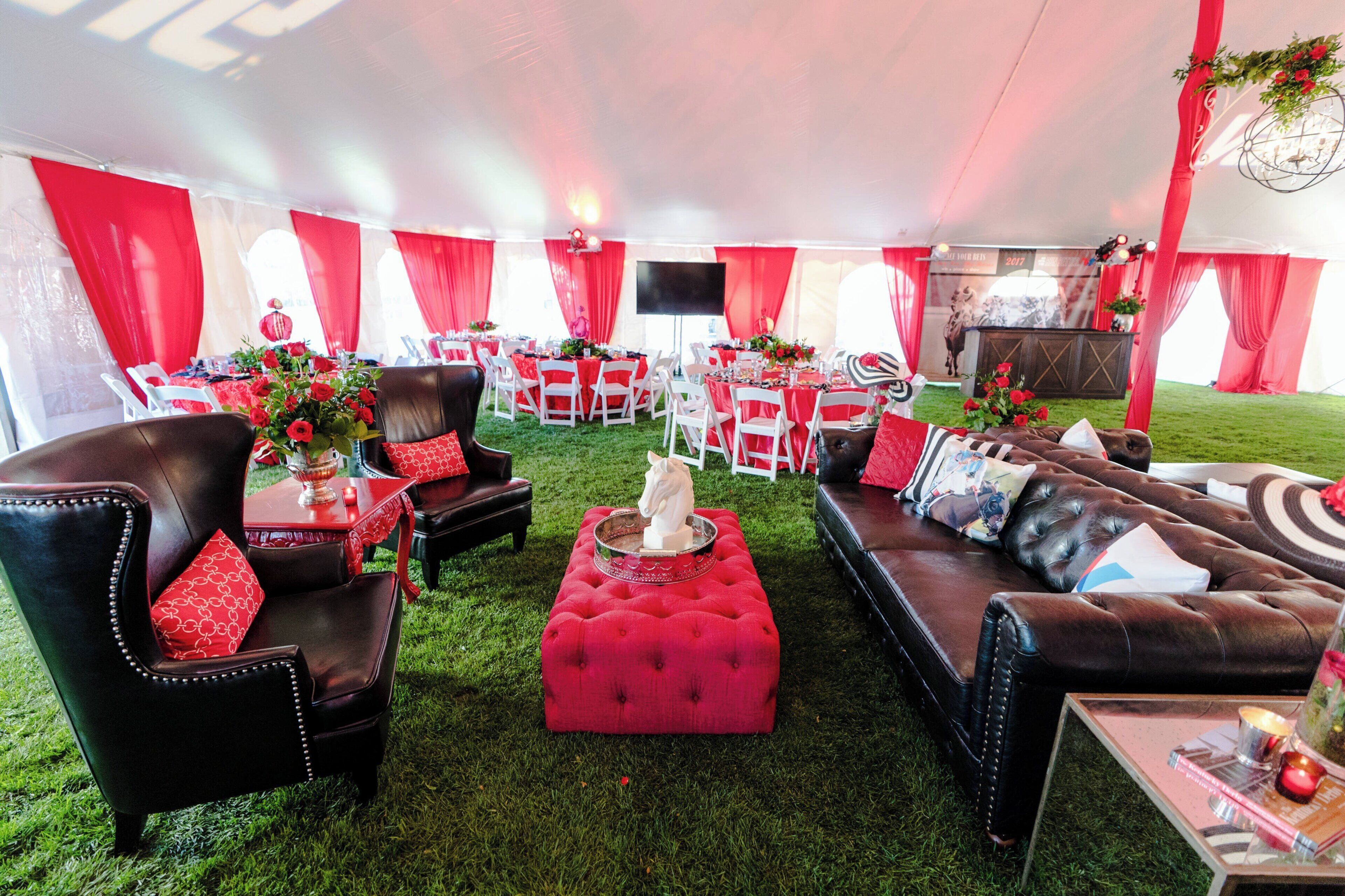 A tented event space with red and white decor, plush seating, and a central stage area.