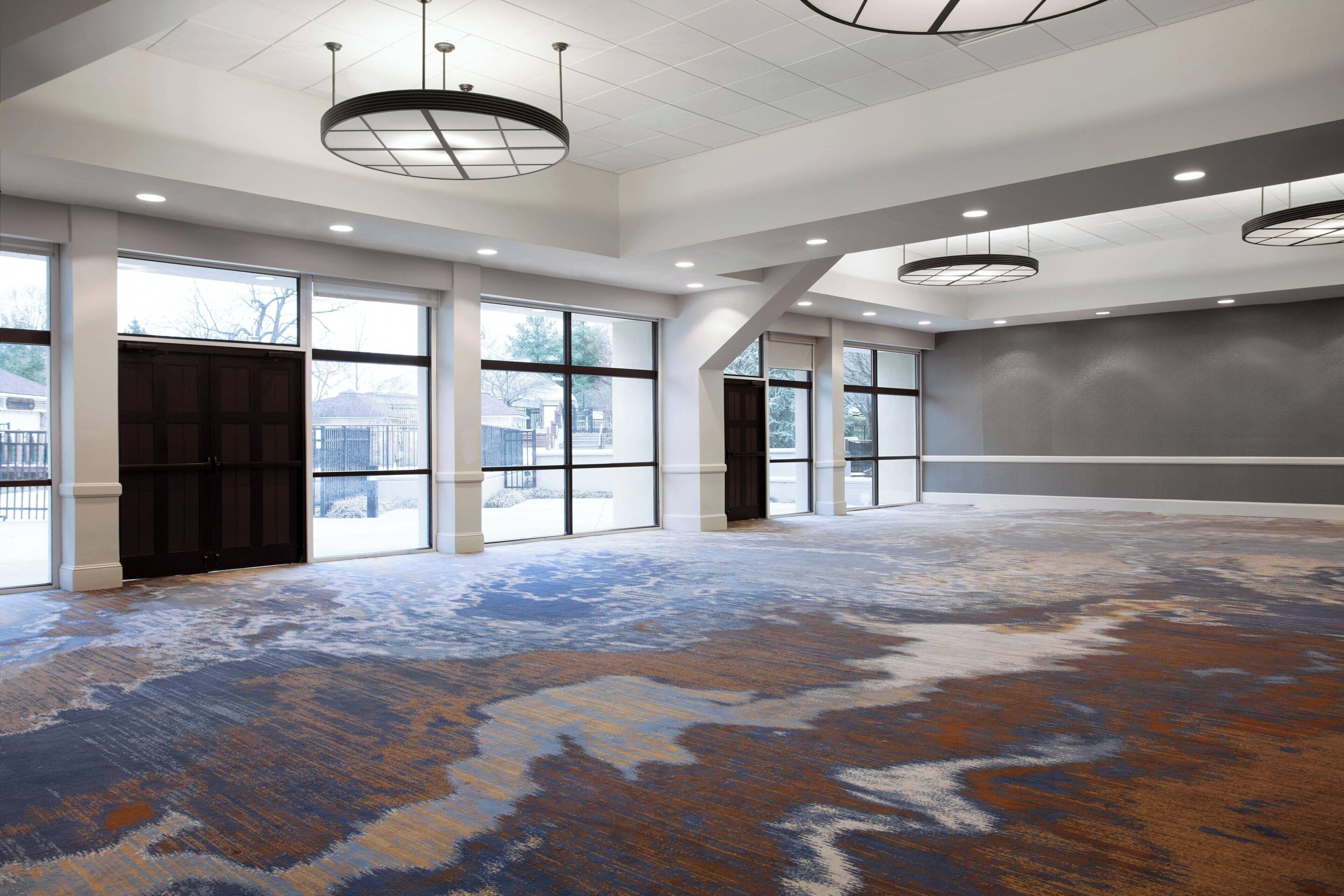 A spacious room with large windows, a patterned carpet, and modern lighting fixtures.