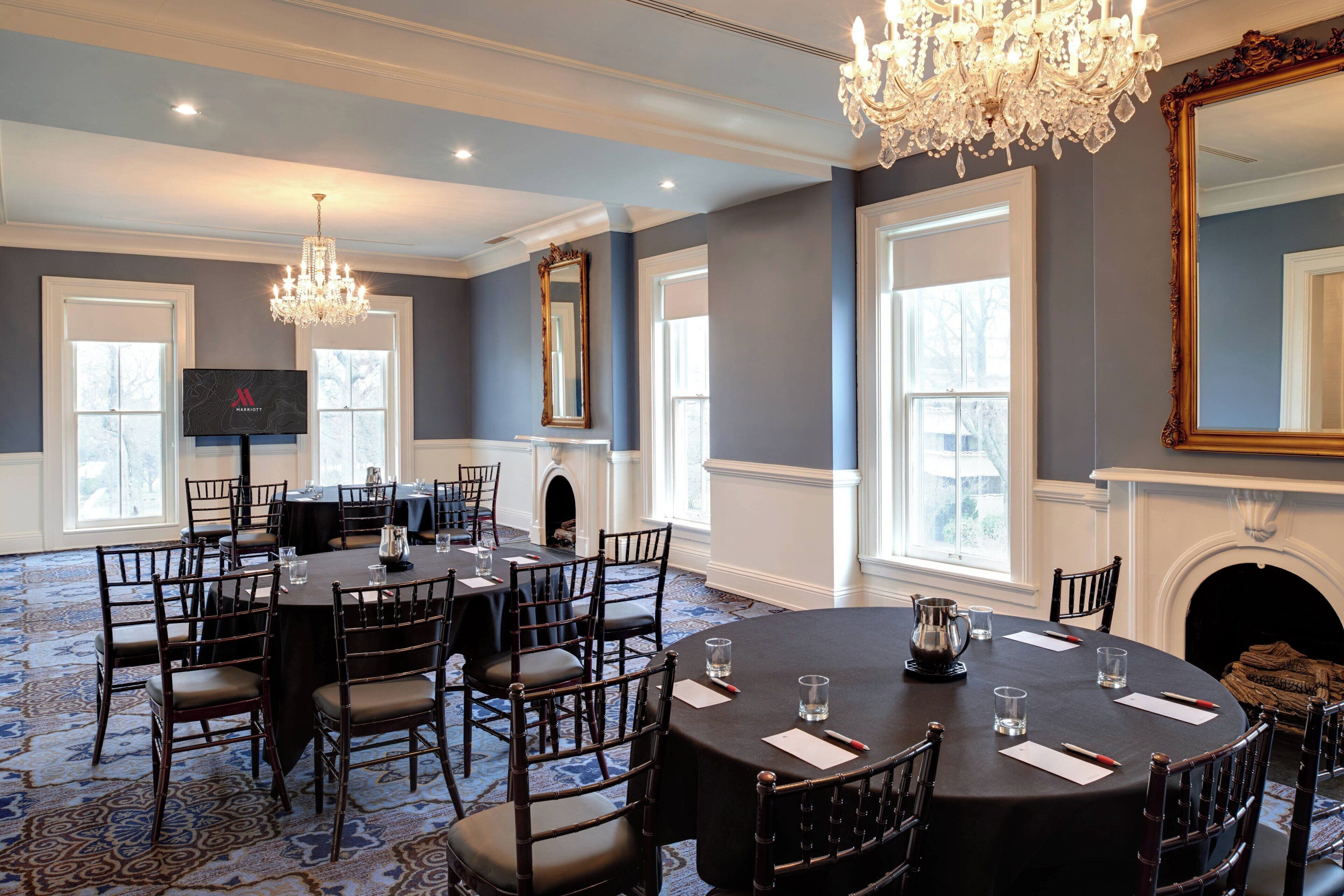 A conference room with round tables, chairs, a chandelier, a fireplace, and large windows.