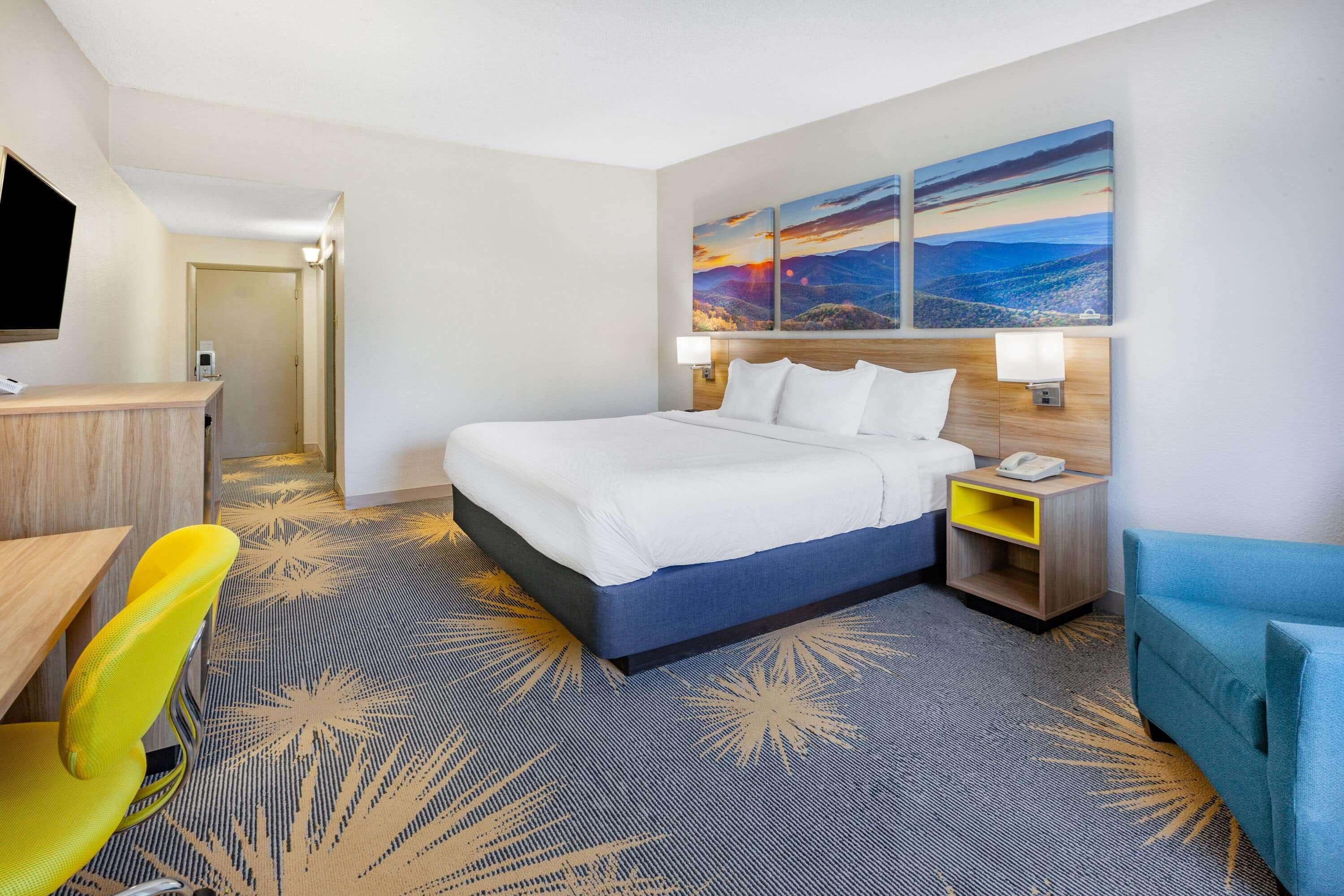 A hotel room with a bed, a desk, a chair, a nightstand, and a wall-mounted TV.