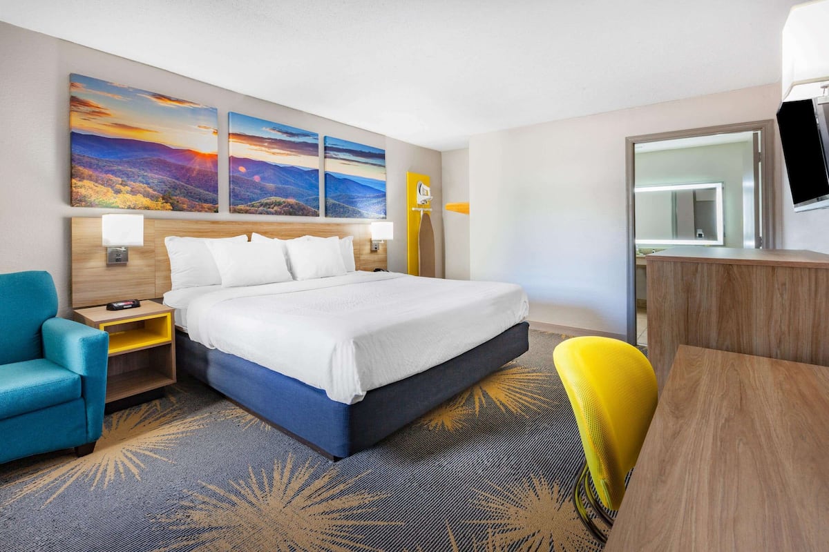 A hotel room with a large bed, a desk, a chair, and artwork on the wall.