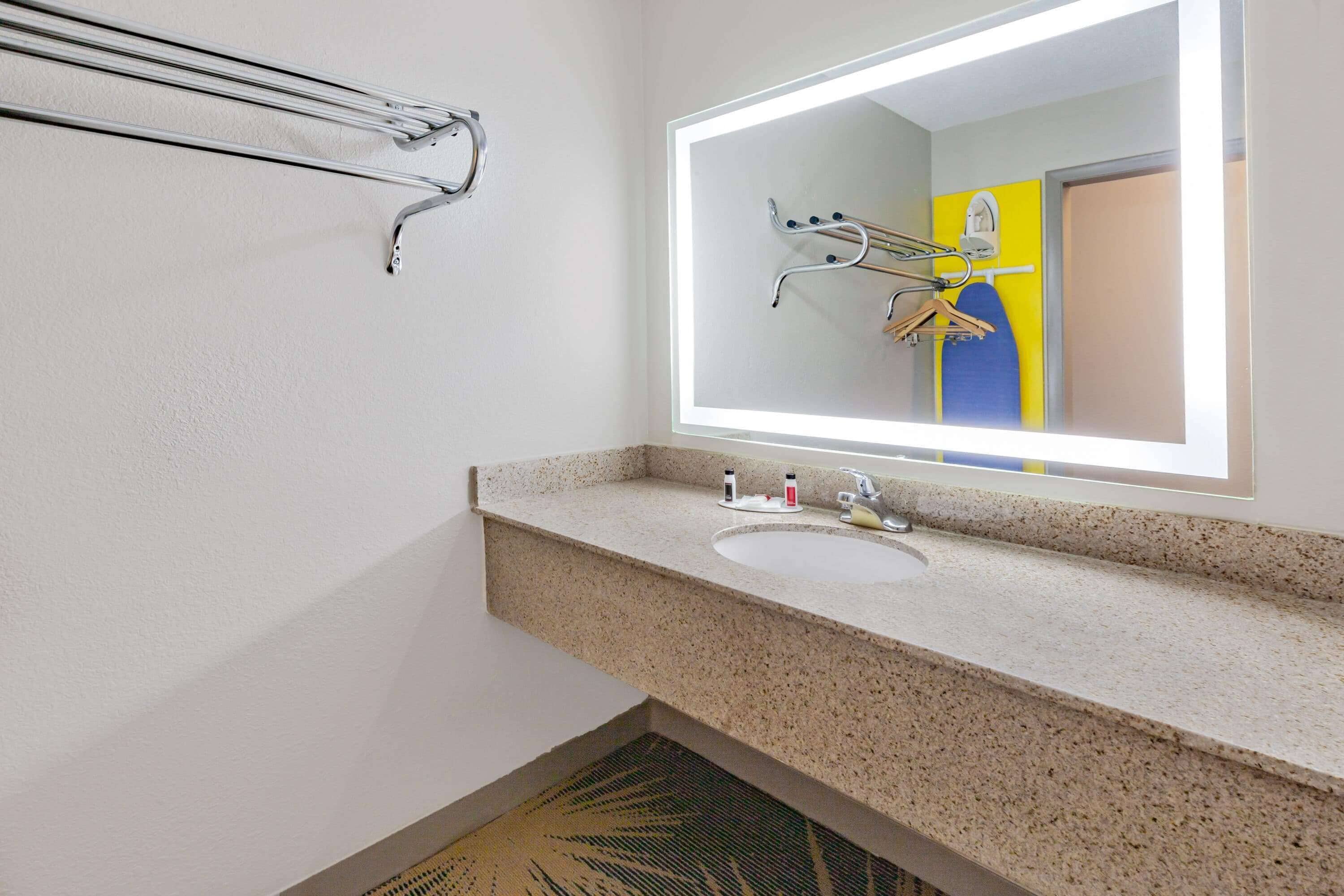 A bathroom with a granite countertop sink, a mirror with integrated lighting, and a towel rack.
