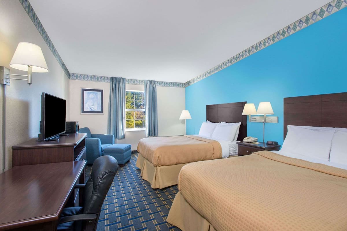 A hotel room with a desk, television, two beds, and a window with curtains.