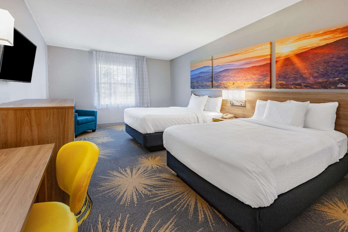 A hotel room with two beds, a desk, a chair, and a large painting on the wall.