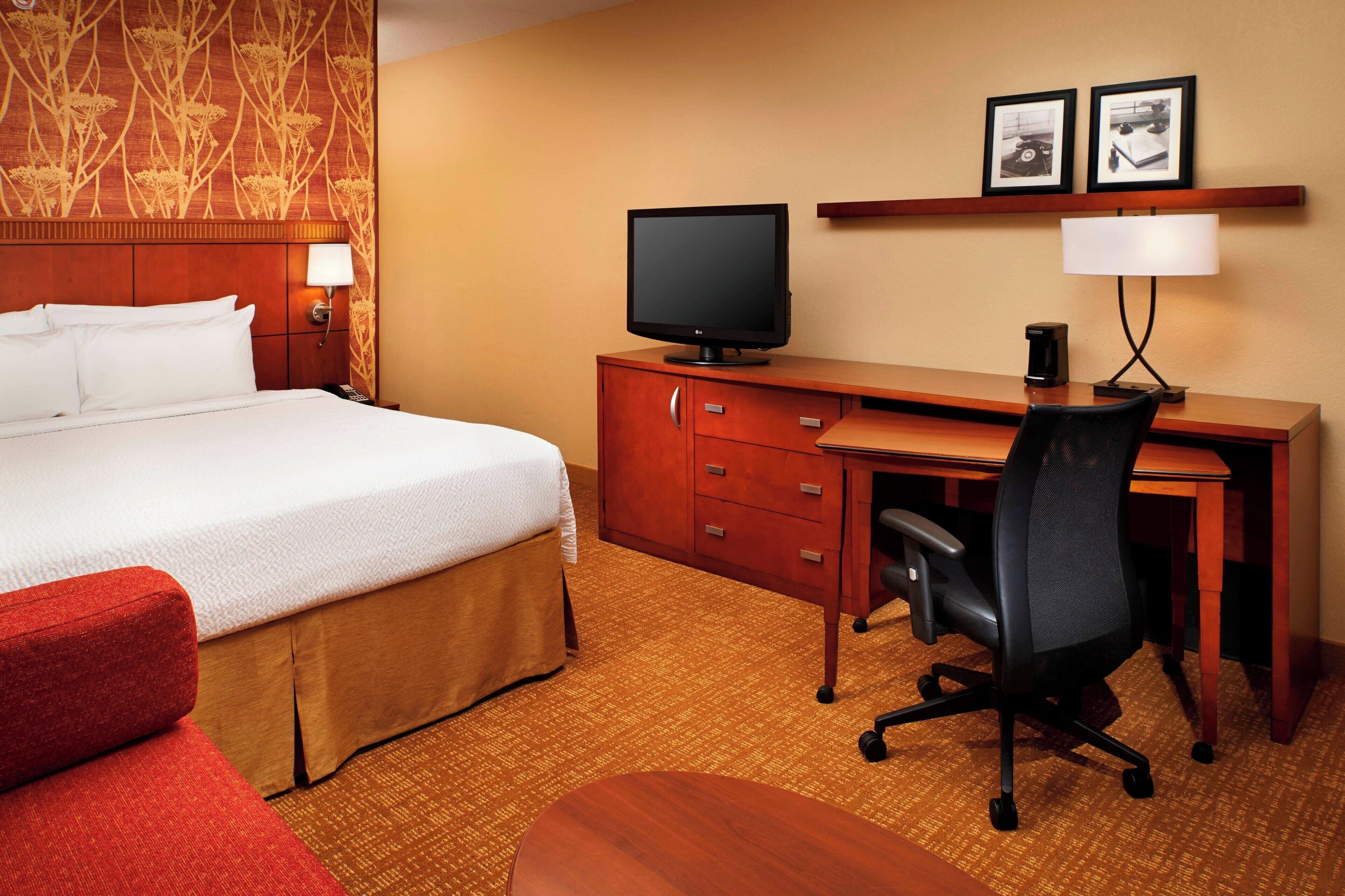 A hotel room with a bed, desk, chair, television, and two framed pictures on the wall.