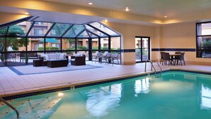 An indoor swimming pool with a glass-enclosed area, lounge chairs, and a dining table. - Courtyard by Marriott Columbus Worthington (Columbus)