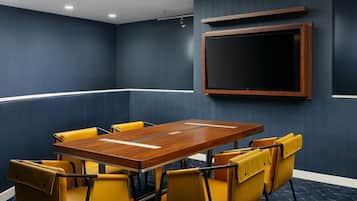 A conference room with a wooden table and yellow chairs, a mounted TV, and dark blue walls.