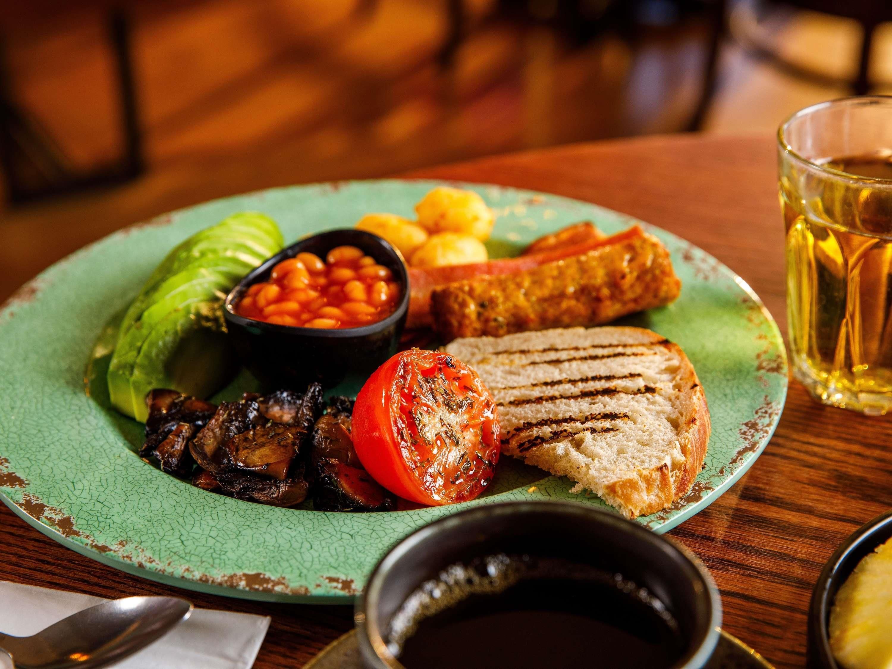 A plate with grilled vegetables, beans, and bread, accompanied by a glass of beer and a cup of coffee.