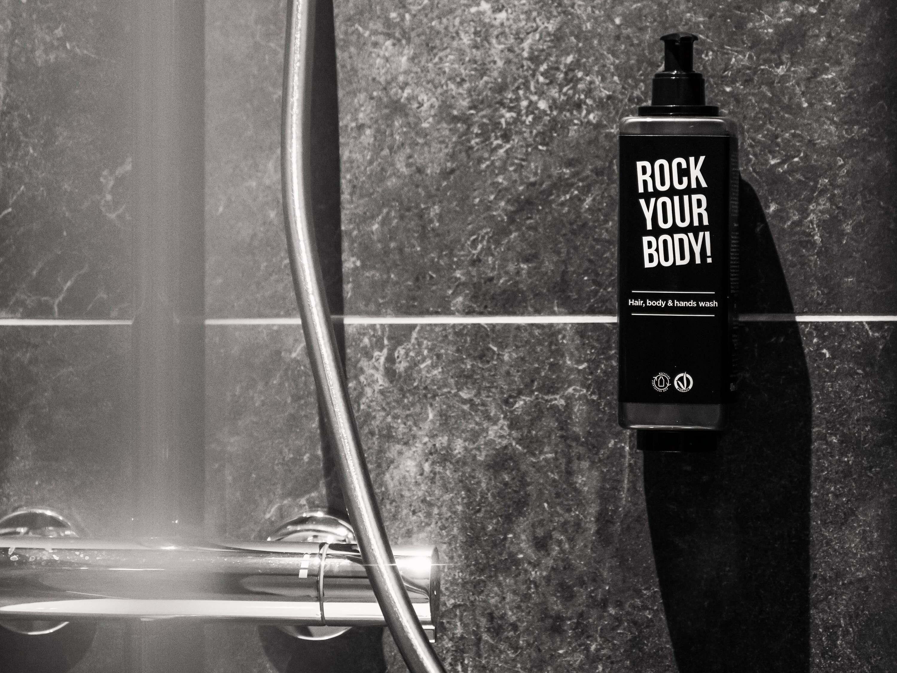 A bathroom with a shower, a towel rack, and a bottle of body wash.