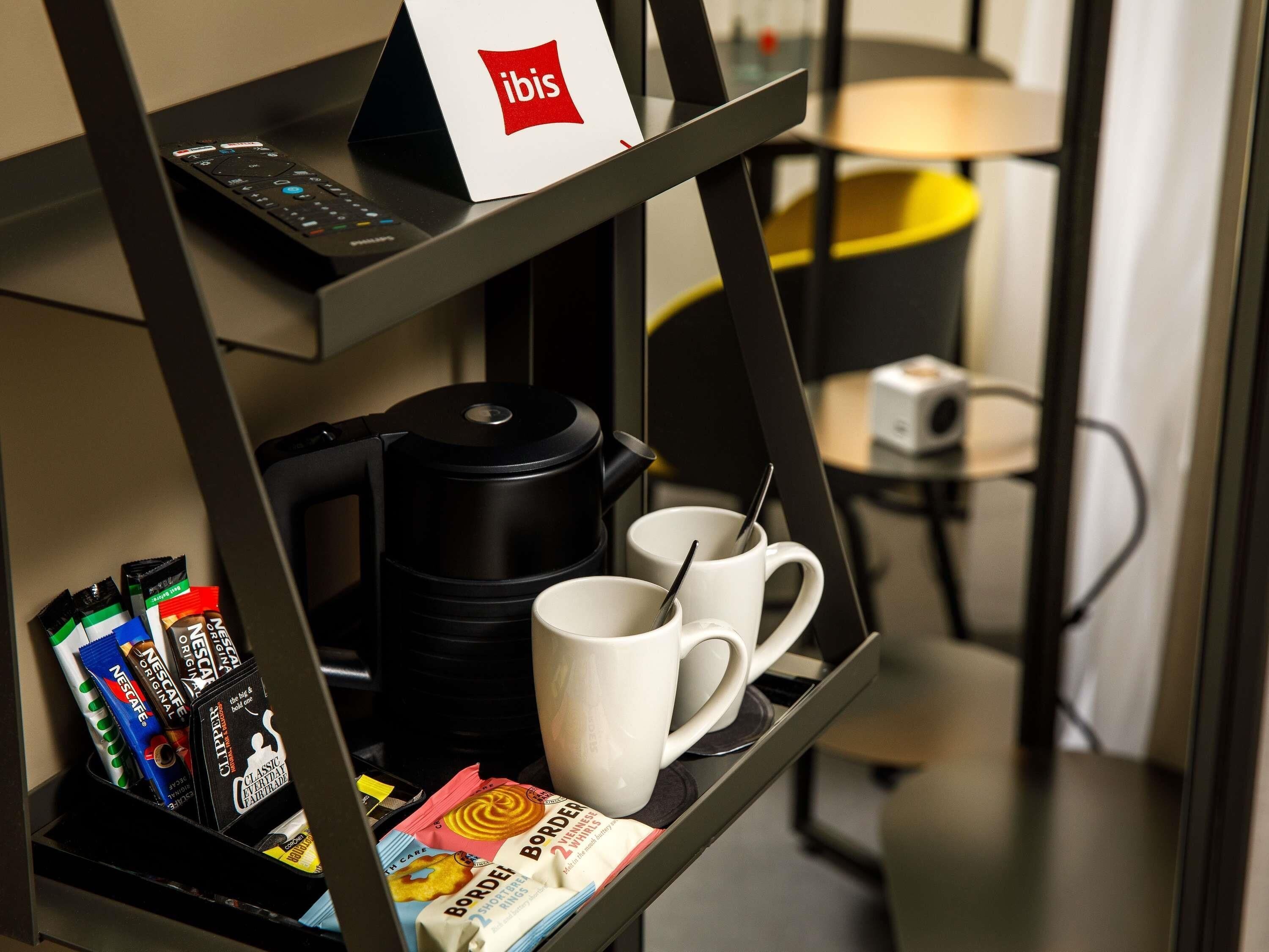 A coffee station with a coffee maker, two white mugs, and various coffee pods.
