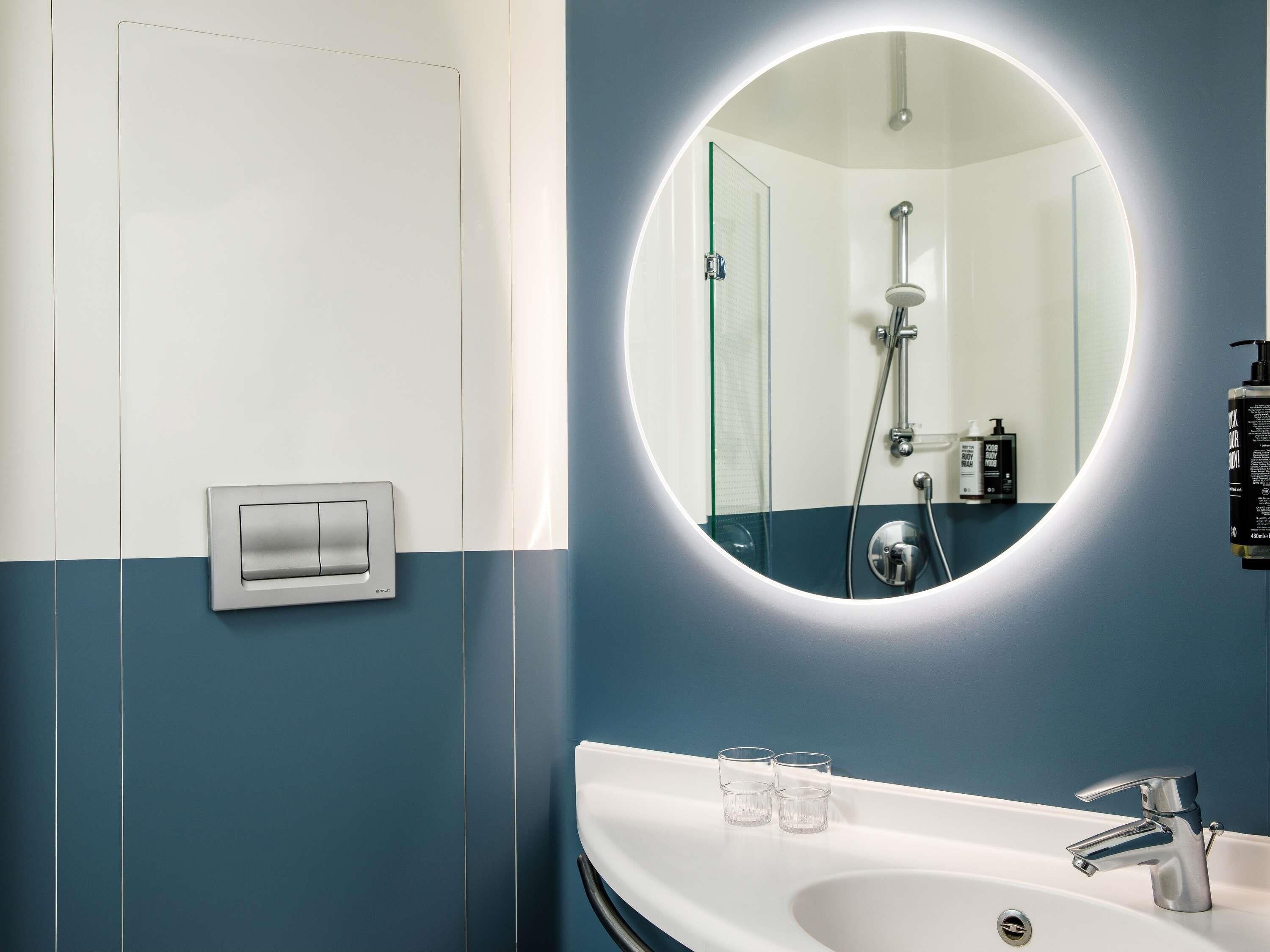 Une salle de bain moderne avec un lavabo blanc, deux verres, un miroir et une douche.