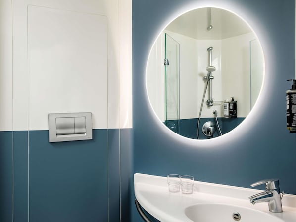 A modern bathroom with a white sink, two glasses, a mirror, and a shower. - ibis London Greenwich (London)