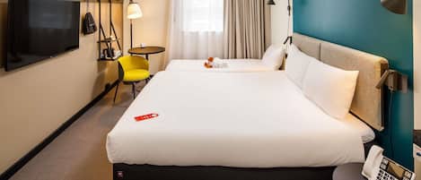 Habitación de hotel con una cama grande, teléfono en la mesita de noche, televisión, una pequeña mesa, una silla y una ventana con cortinas.