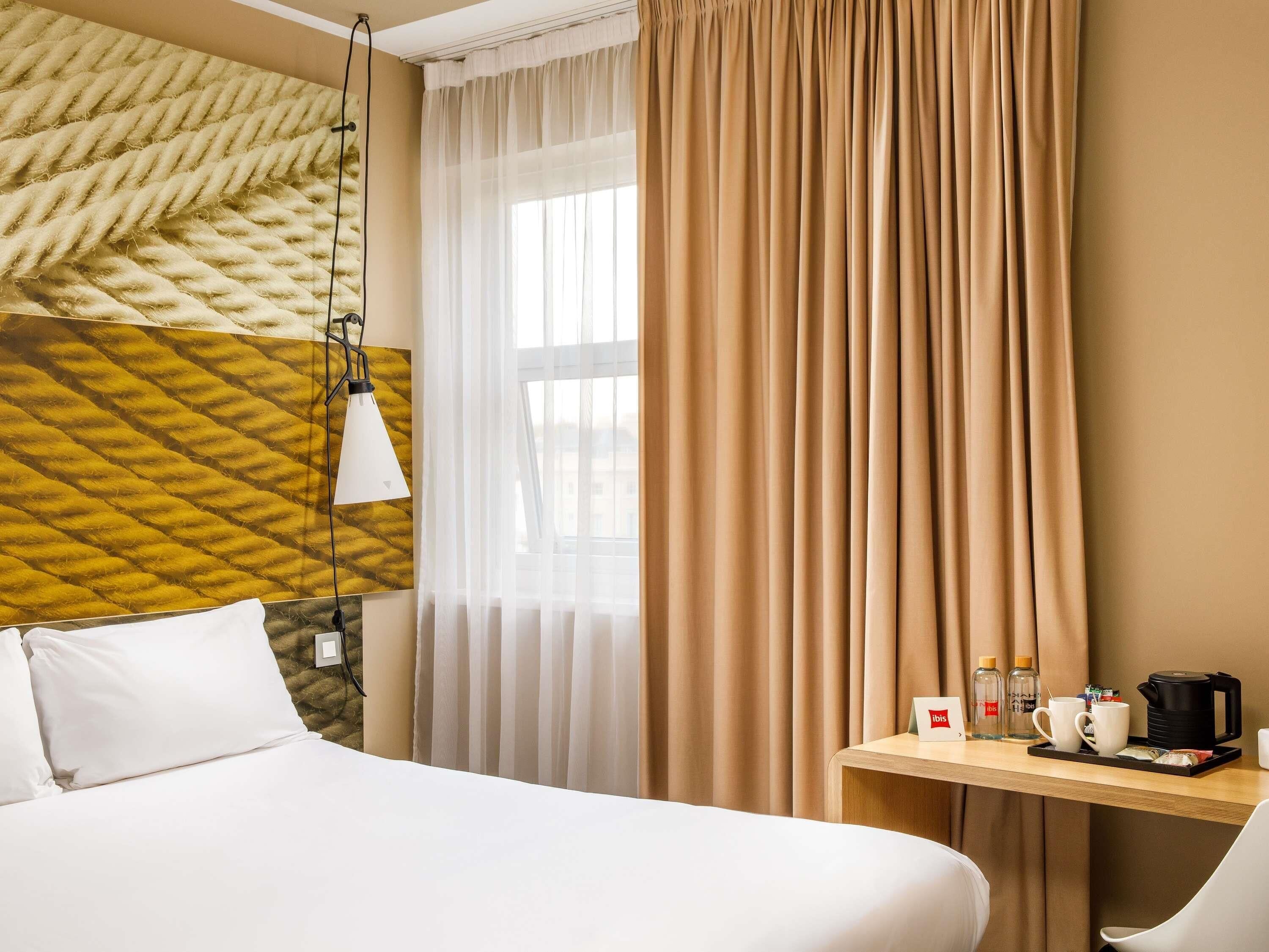 A hotel room with a bed, a desk with a coffee maker, and a view of the city through the window.