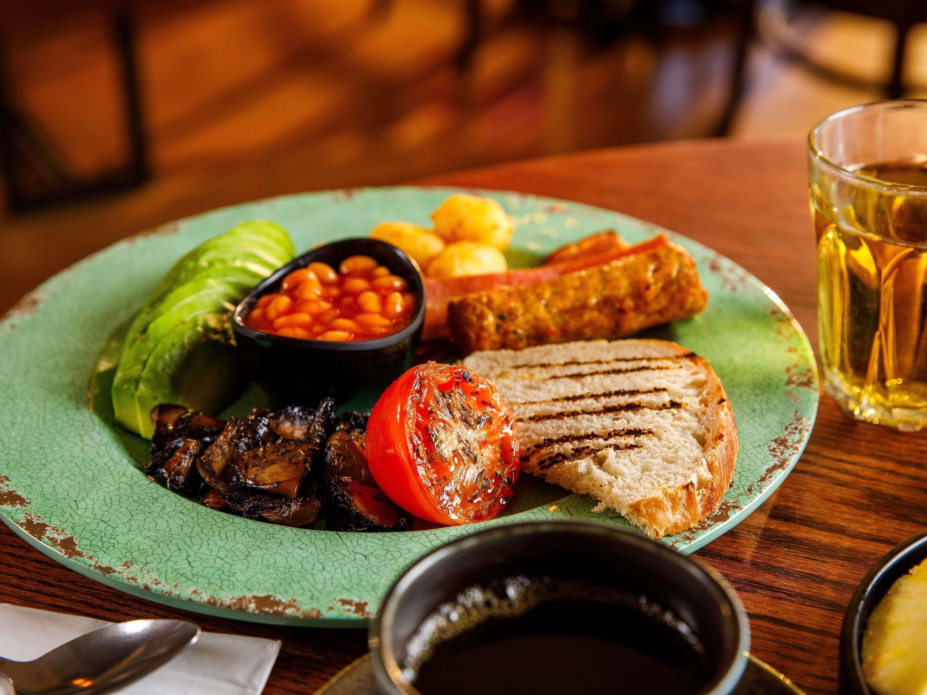 Ein Teller mit gegrilltem Gemüse, Bohnen und Brot, dazu ein Glas Bier und eine Tasse Kaffee.