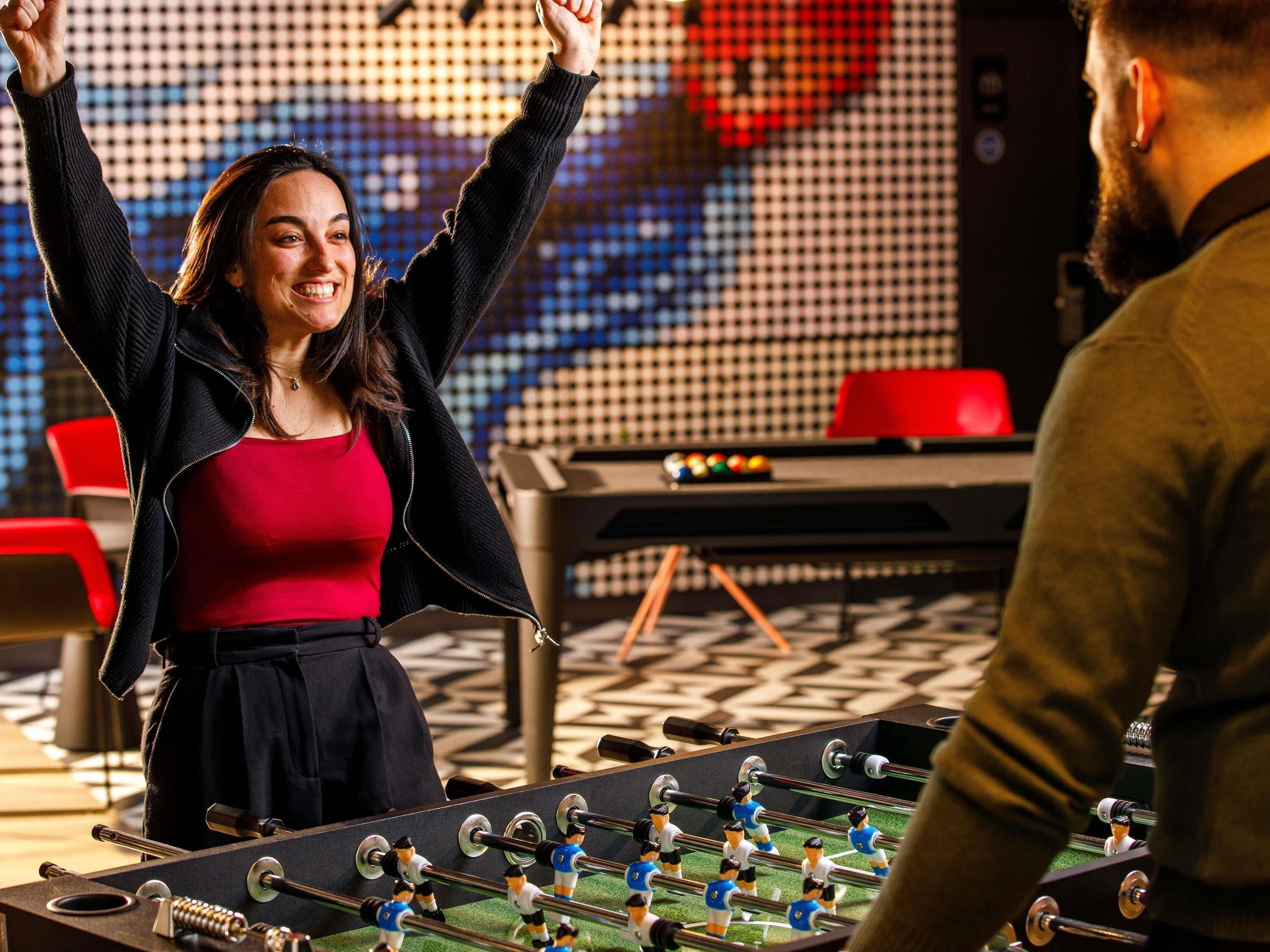 Een tafelvoetbaltafel in een ruimte met een kamer met een patroon vloer en rode stoelen.