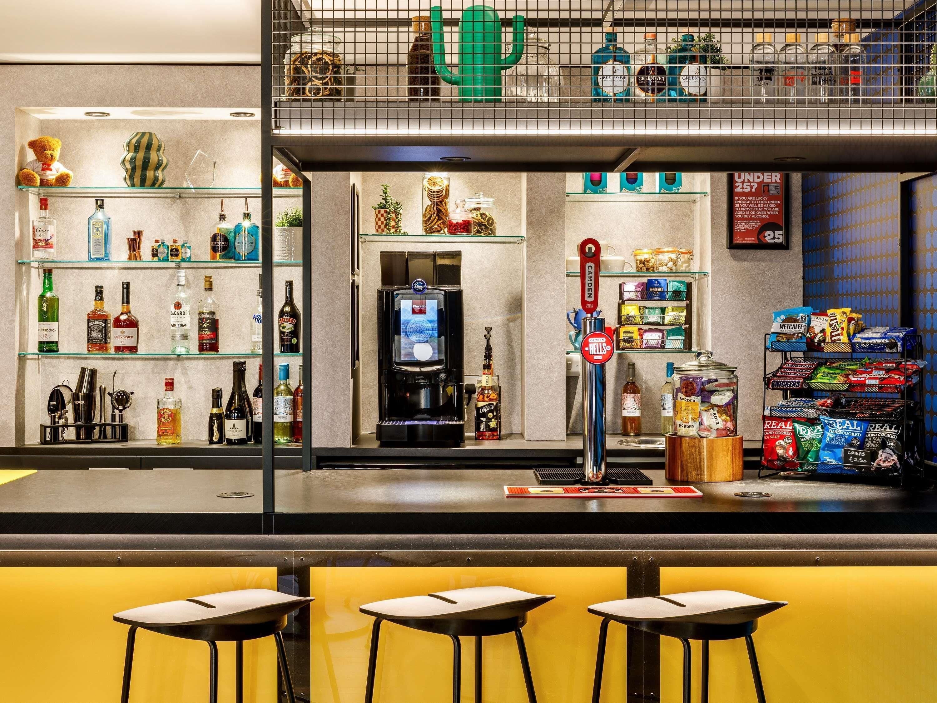 A bar area with stools, shelves of liquor bottles, a coffee machine, and snack dispensers.