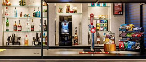 A bar area with stools, shelves of liquor bottles, a coffee machine, and snack dispensers.