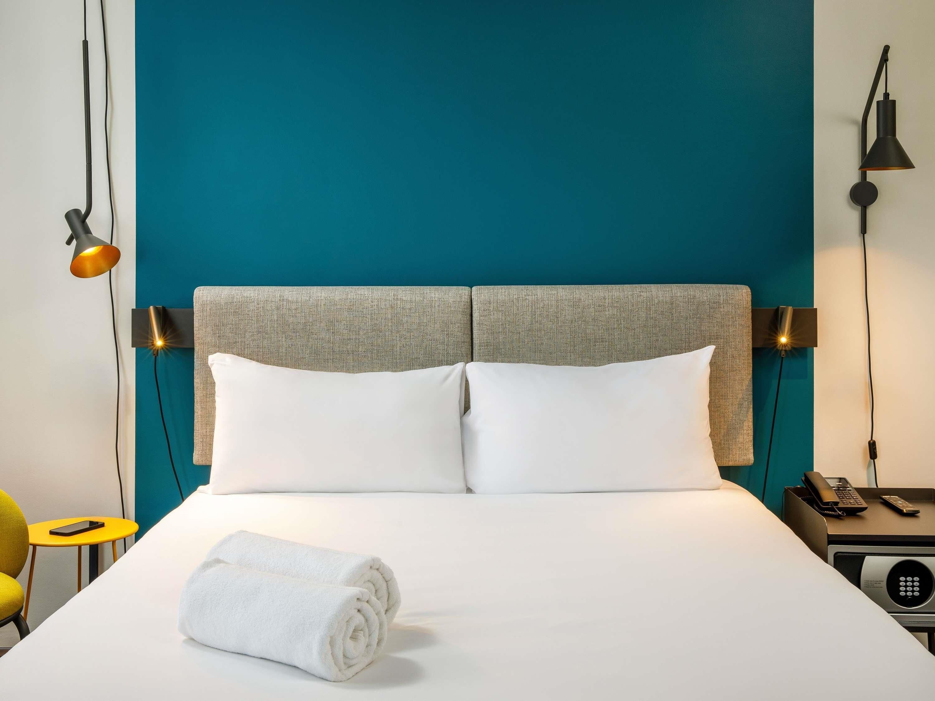 A hotel room with a bed, two bedside lamps, a telephone, and a small table with a remote control.