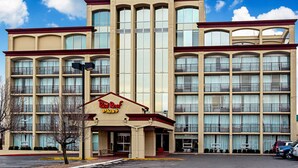 A Red Roof Plus hotel with a symmetrical facade, multiple balconies, and a clear sky.