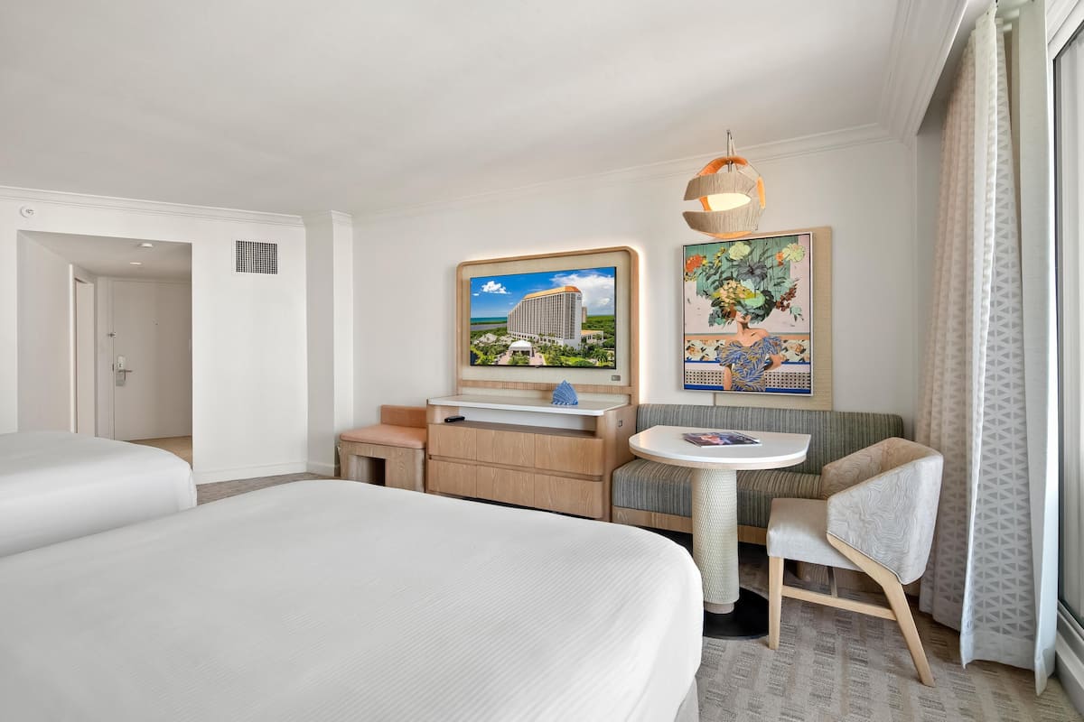 Habitación de hotel con cama, escritorio, silla, mesa redonda, televisor y obras de arte en las paredes.
