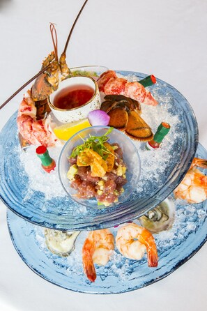 A seafood platter with various types of seafood, a bowl of salad, and a bottle of sauce on a blue plate. - Signia Hilton Naples Grande Beach Resort (Naples)