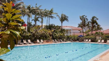 Relax by the pool surrounded by lush greenery and palm trees, with lounge chairs and umbrellas for a serene escape.