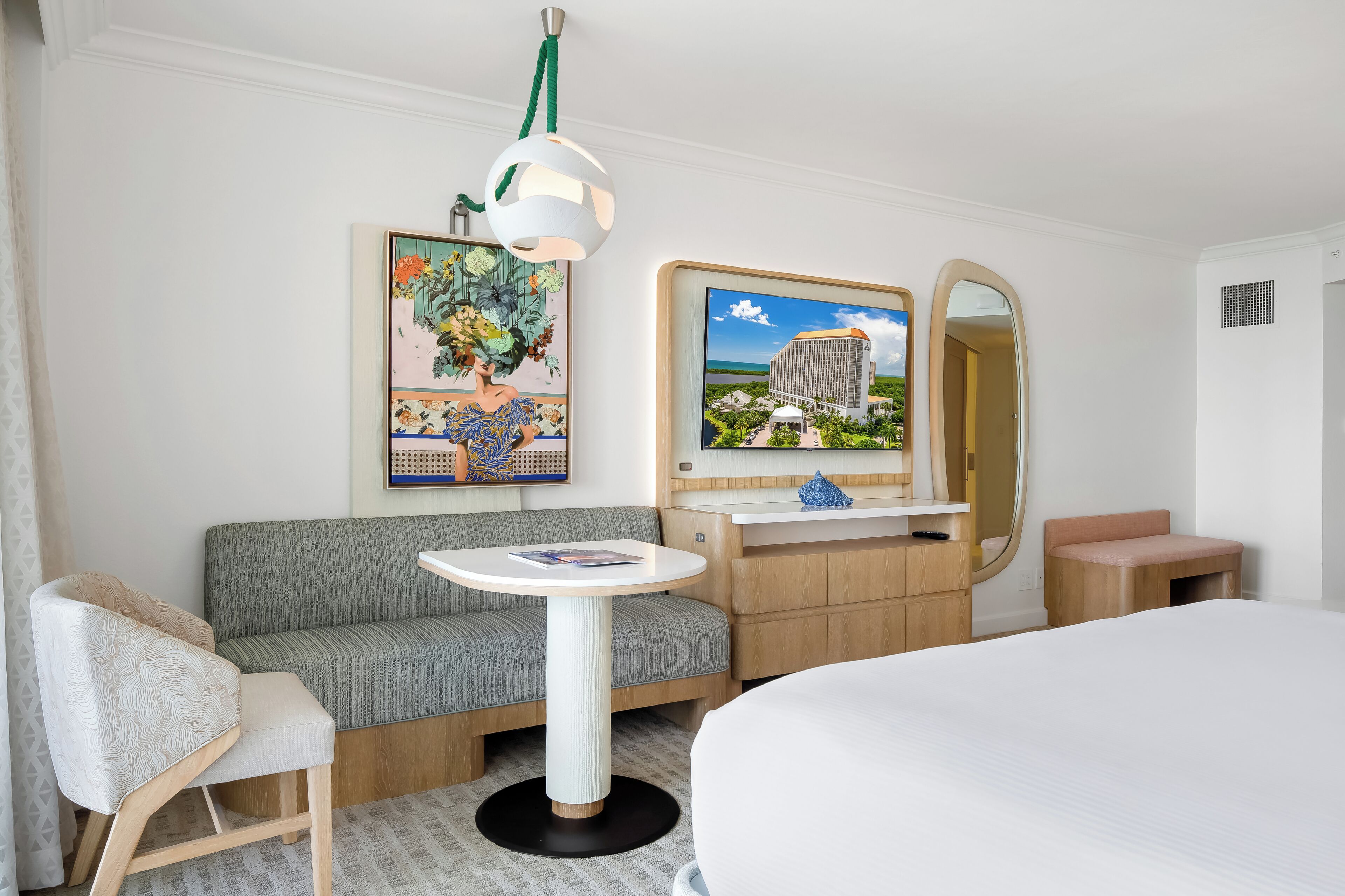 Habitación de hotel con sofá, una mesita redonda, cama, espejo y obras de arte en la pared.