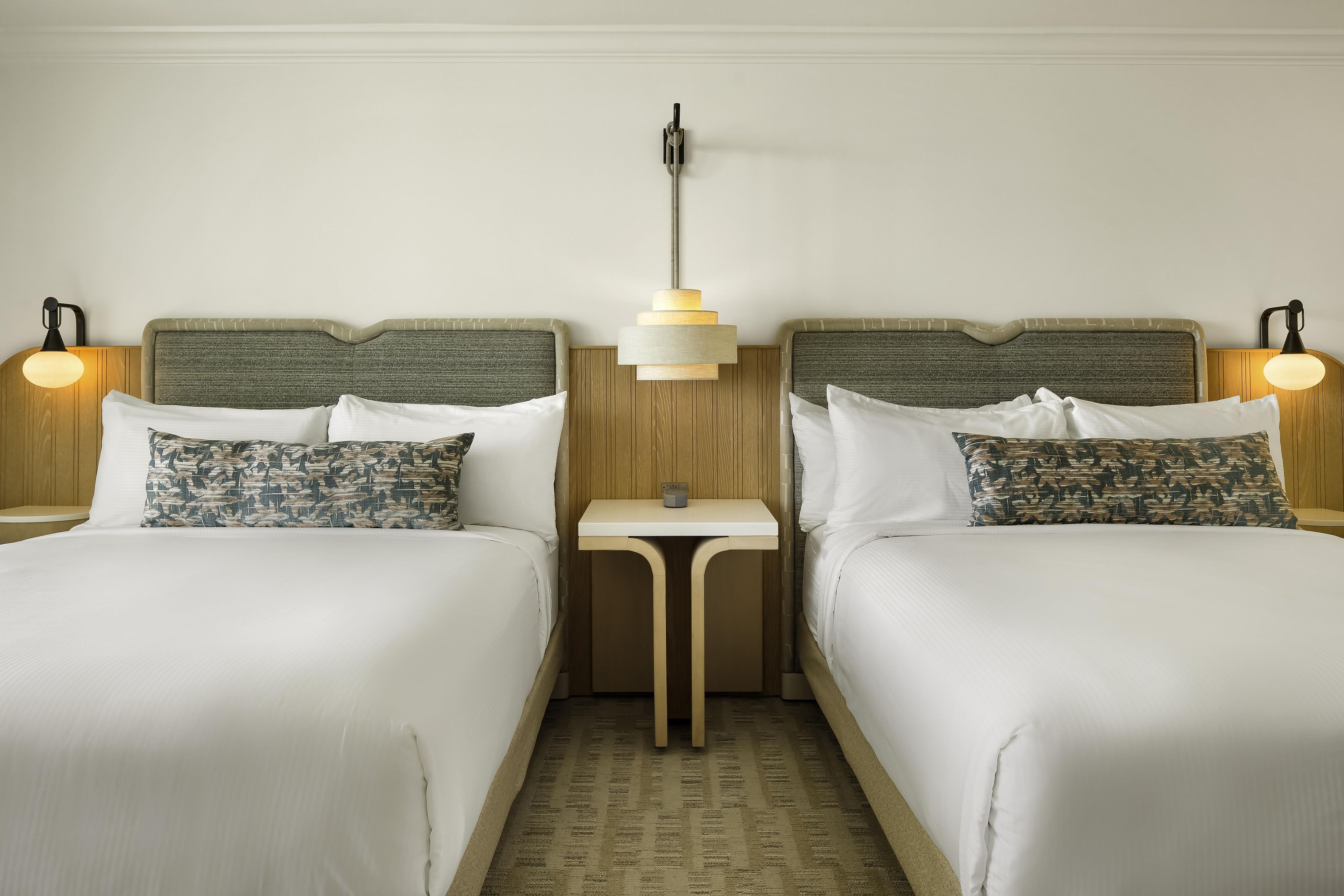 A hotel room with two beds, a small table, and two bedside lamps.