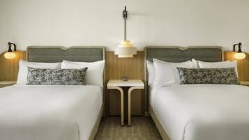 A hotel room with two beds, a small table, and two bedside lamps.